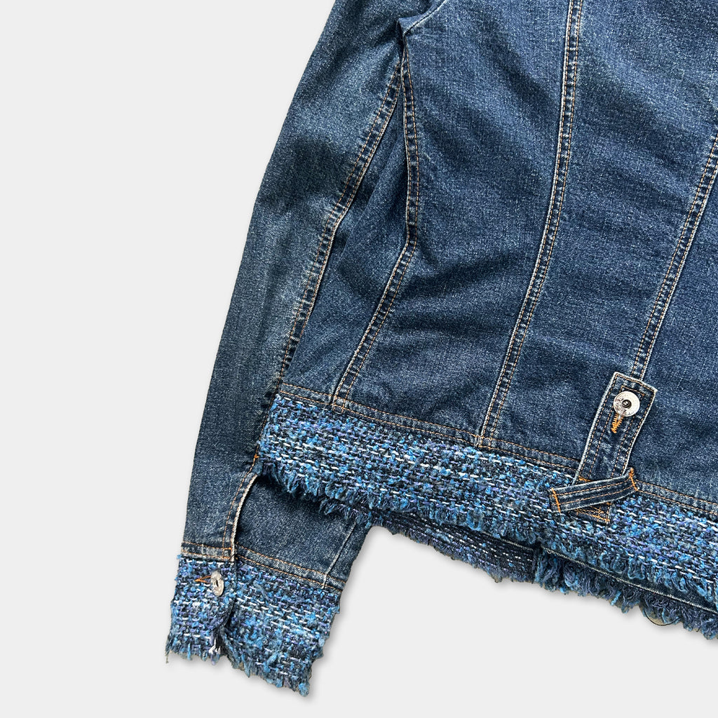 A close-up view of a denim jacket with frayed edges and a frayed hem, showcasing the fabric's texture and details.