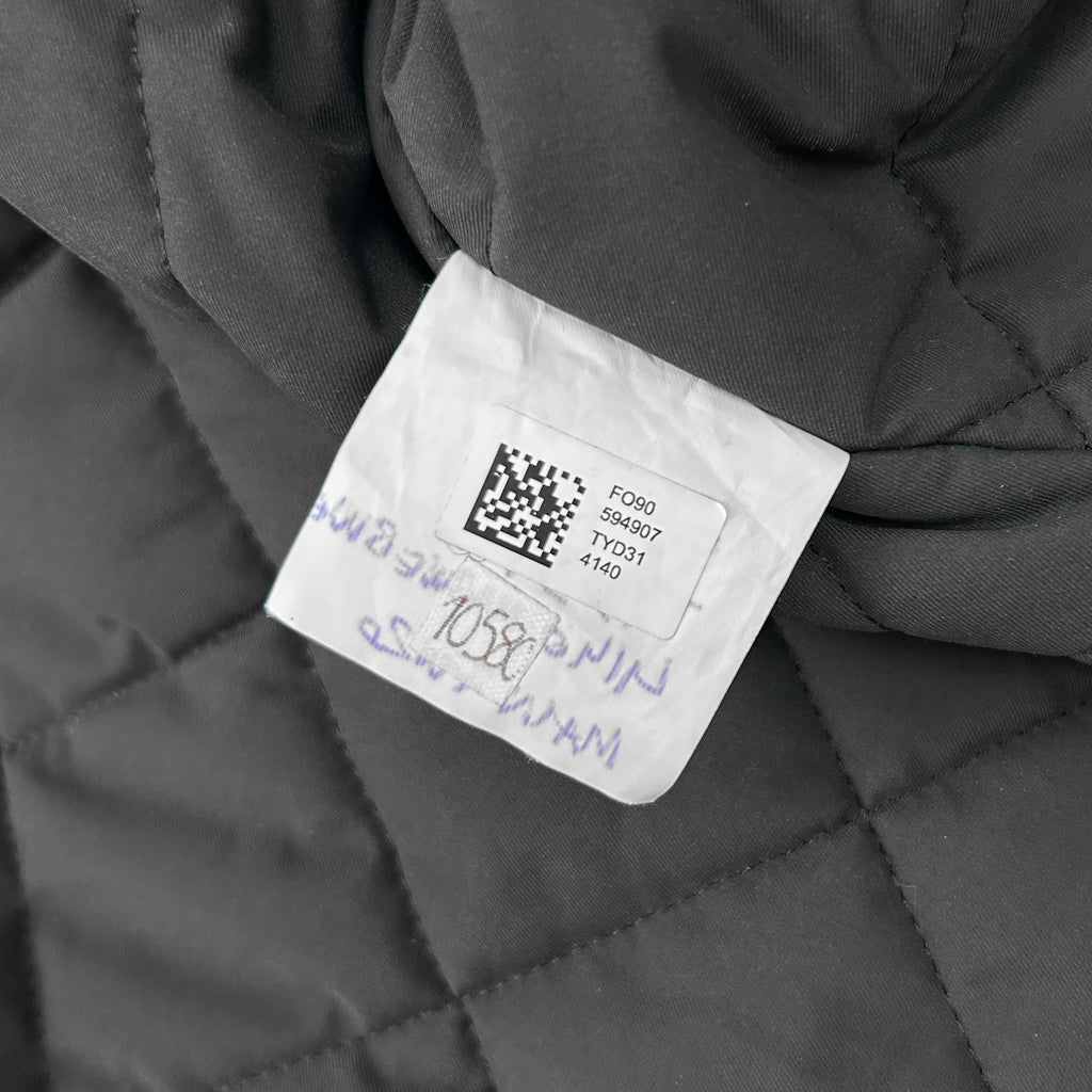 a close-up view of a piece of fabric, possibly a quilted material, with a label attached to it. The label appears to contain some text and a barcode, but the image is not clear enough to transcribe the specific details.