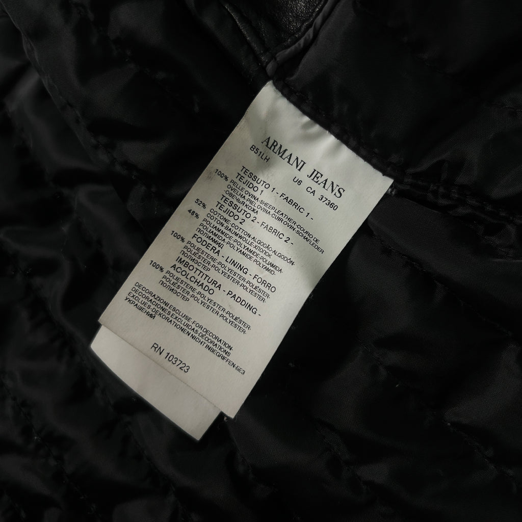 a close-up view of a black fabric, possibly a piece of clothing, with a label attached to it. The label appears to be a label from an Armani Jeans brand, providing information about the product.
