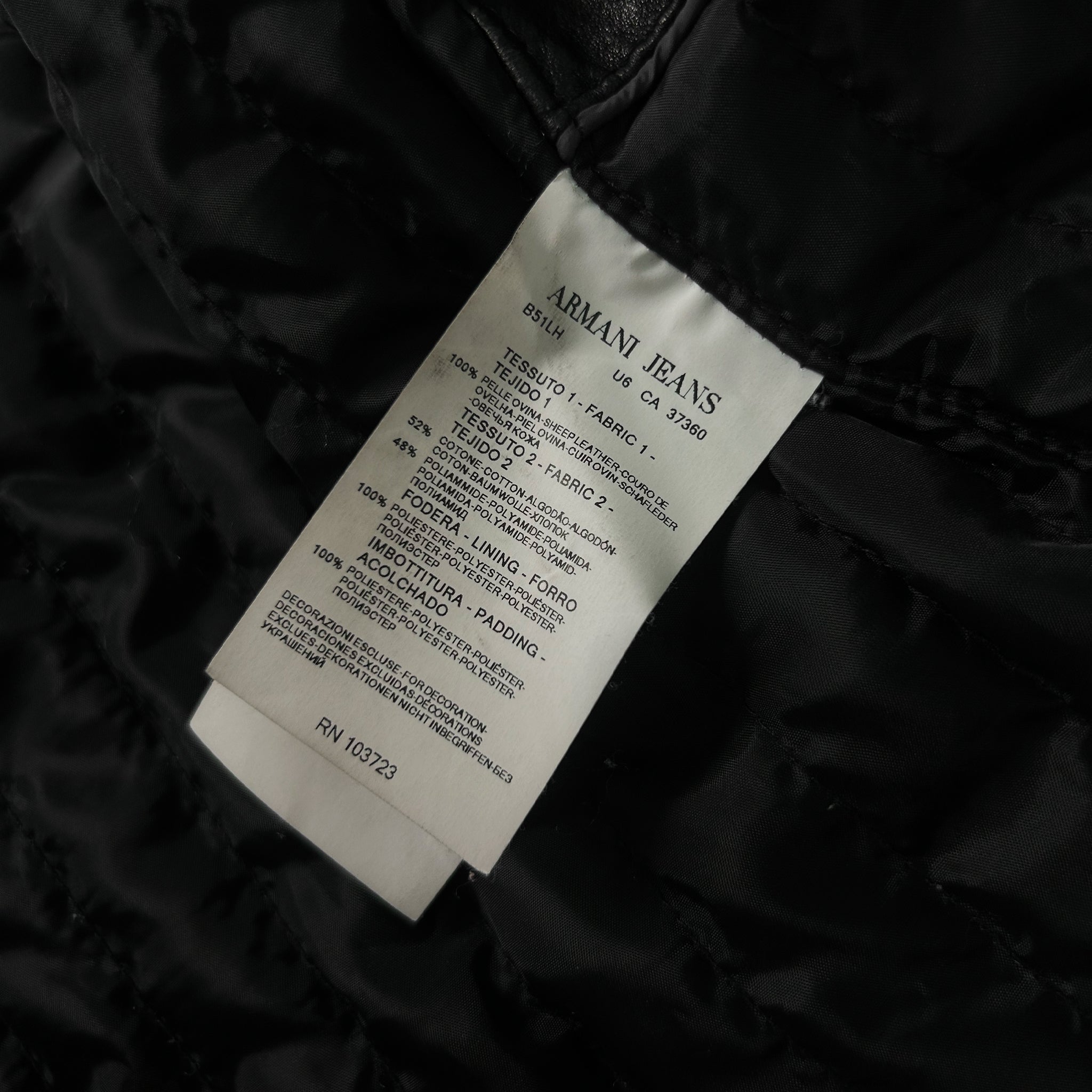 a close-up view of a black fabric, possibly a piece of clothing, with a label attached to it. The label appears to be a label from an Armani Jeans brand, providing information about the product.