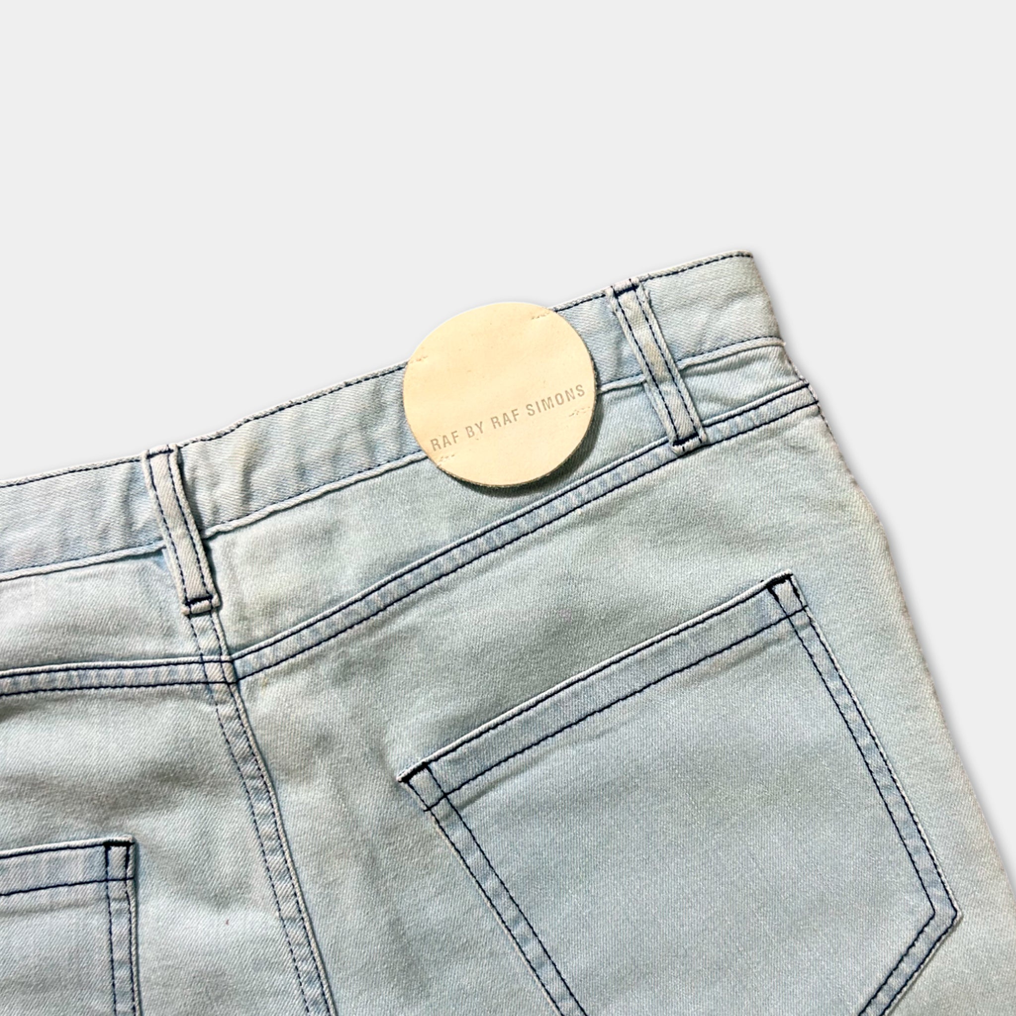 A pair of light blue denim jeans with a round tag attached to the waistband.