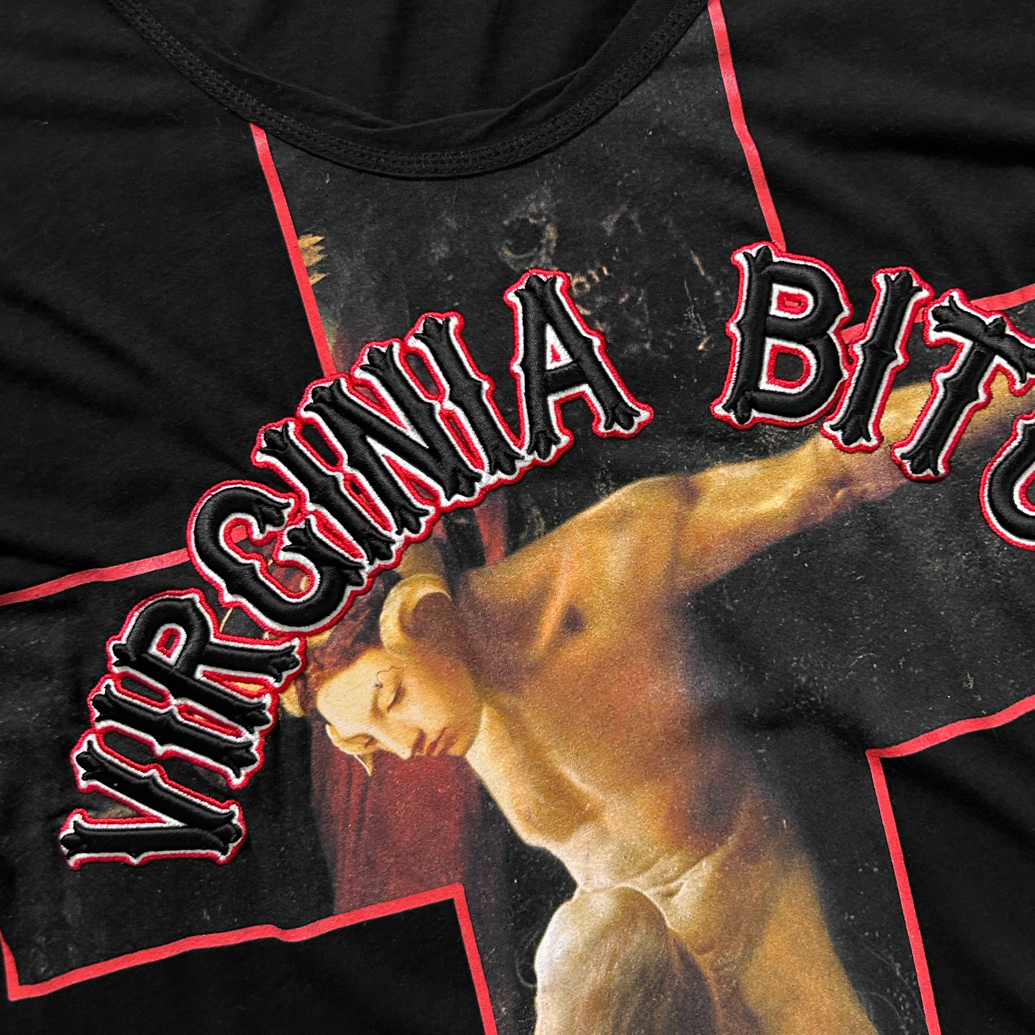 a black t-shirt with a graphic design on it. The design includes a large red cross and a painting of a person. The text "VIRGINIA BIT" is prominently displayed across the t-shirt.