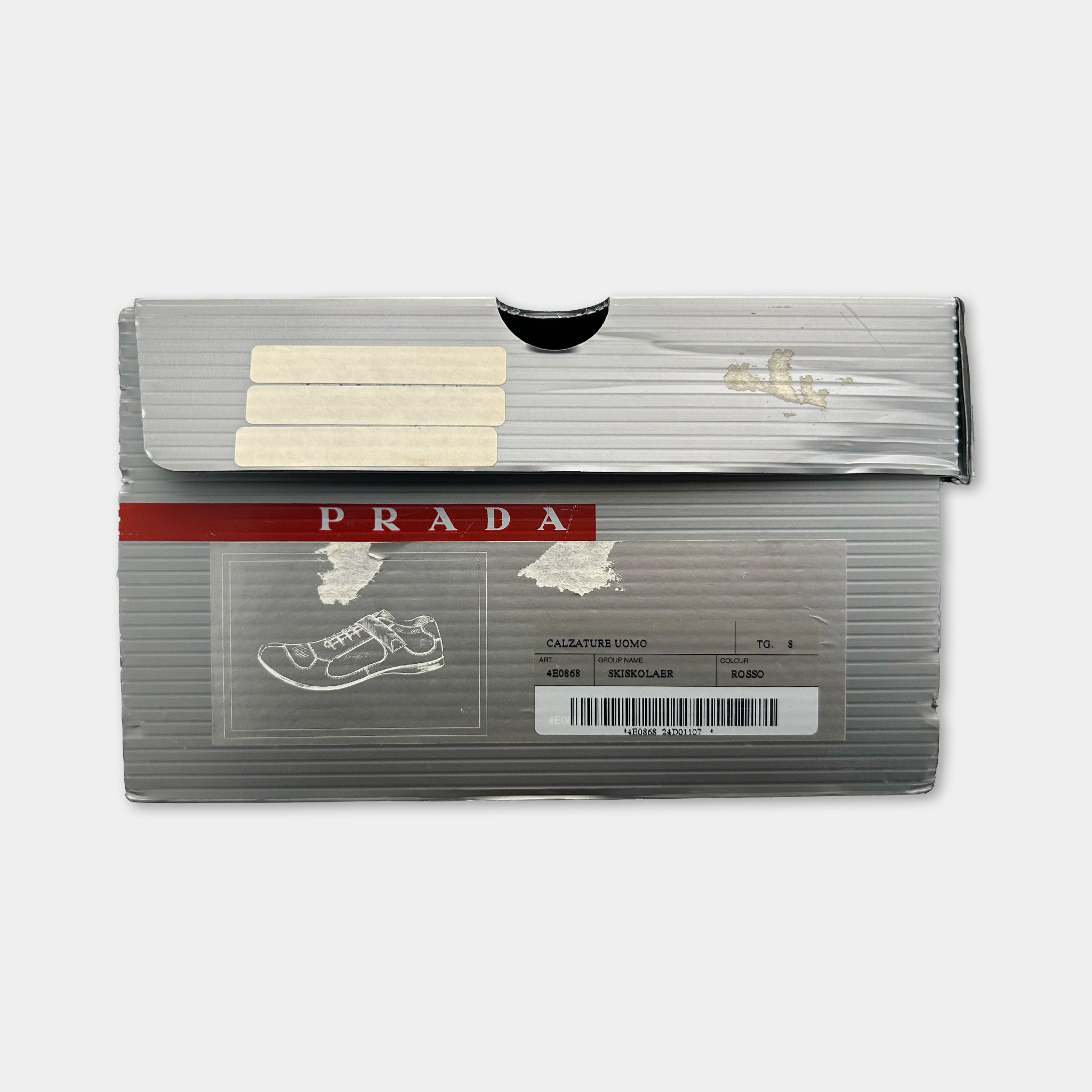 a silver Prada shoe box with a red stripe and a label that includes a picture of a shoe and some text.