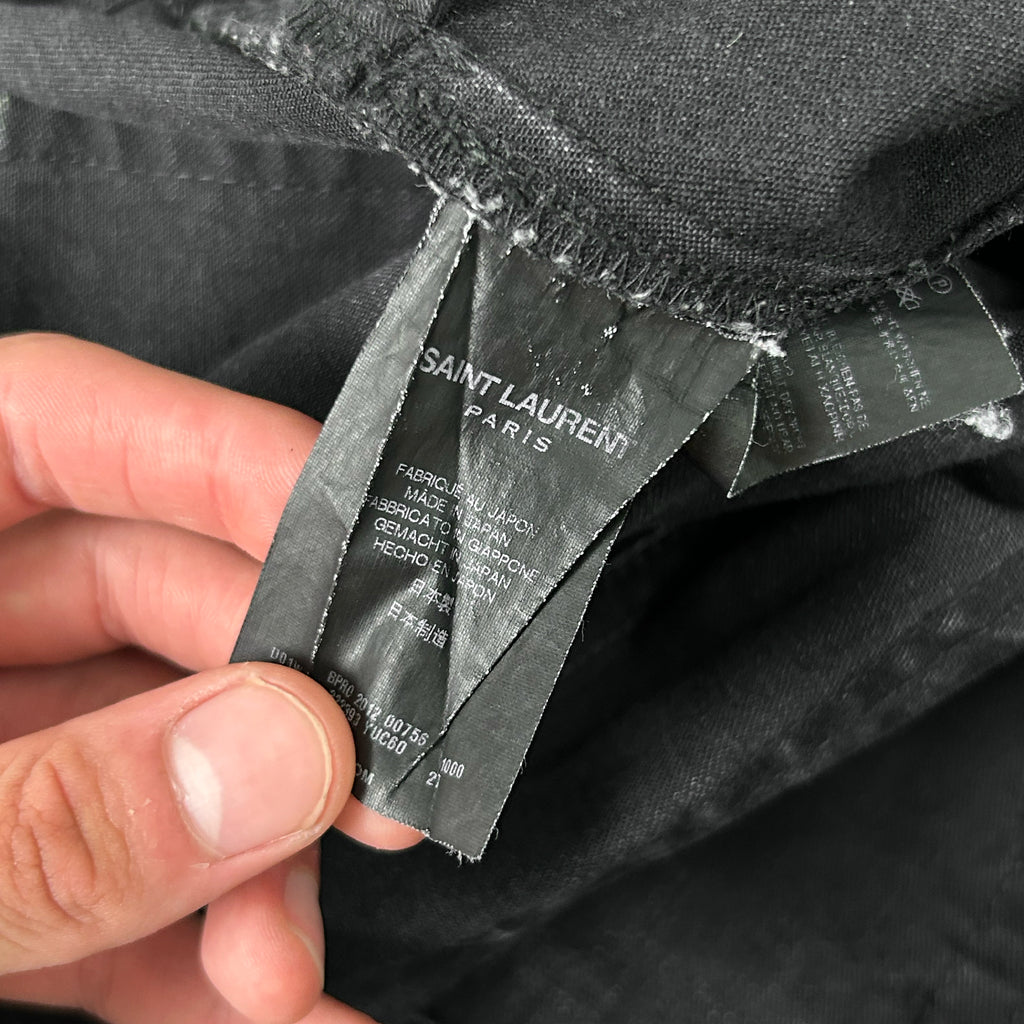 A person's hand holding a black fabric with a label attached to it, which appears to be a label from a clothing brand.