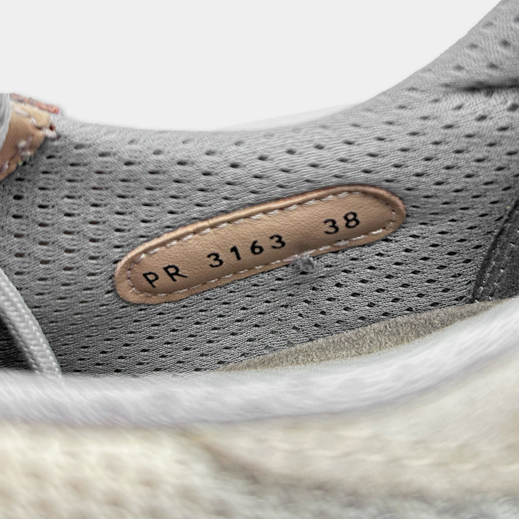 A close-up view of a gray and white shoe, with a small label on the side of the shoe displaying the number "38".