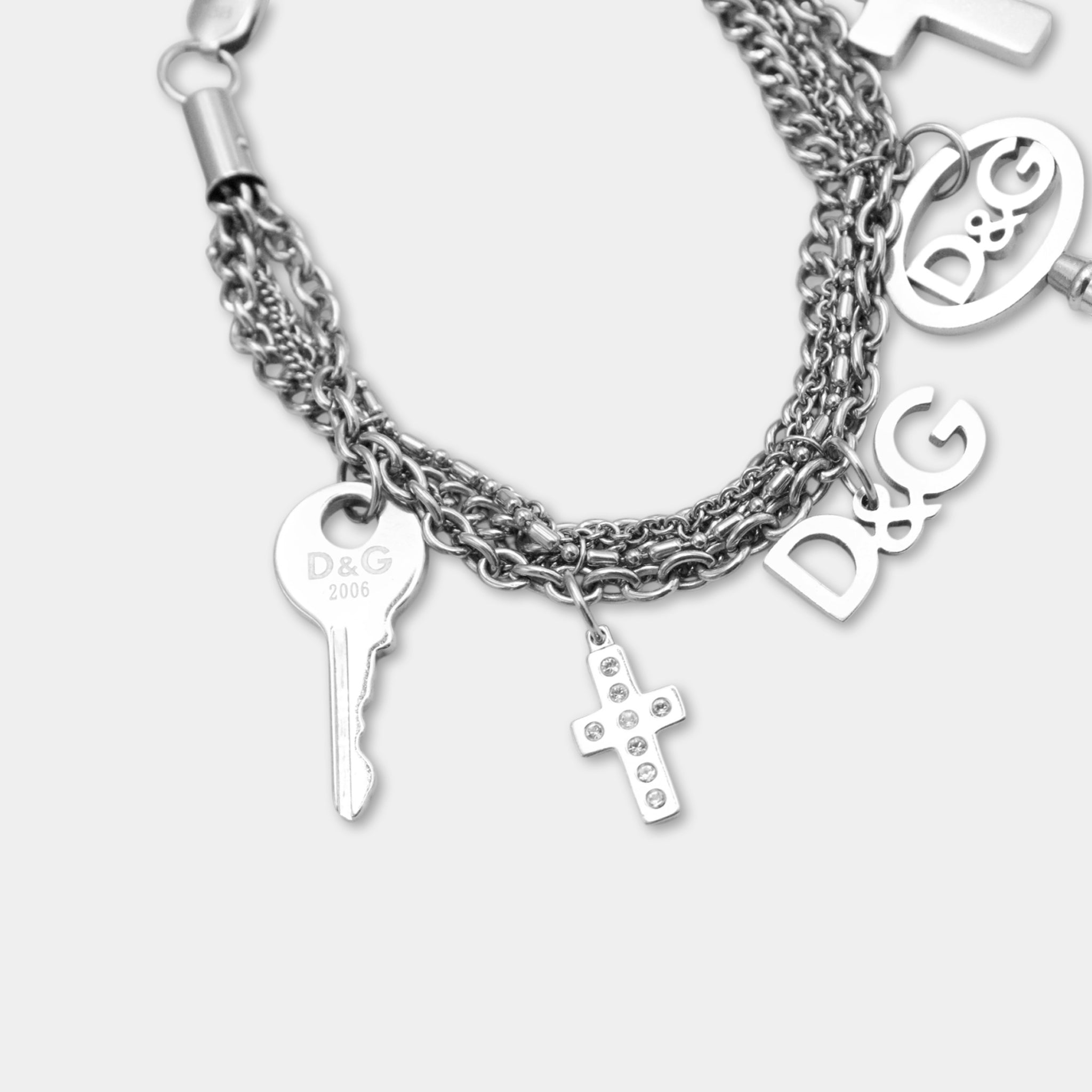 A silver-colored bracelet with various charms, including a key, a cross, and the letters 'D&G'.