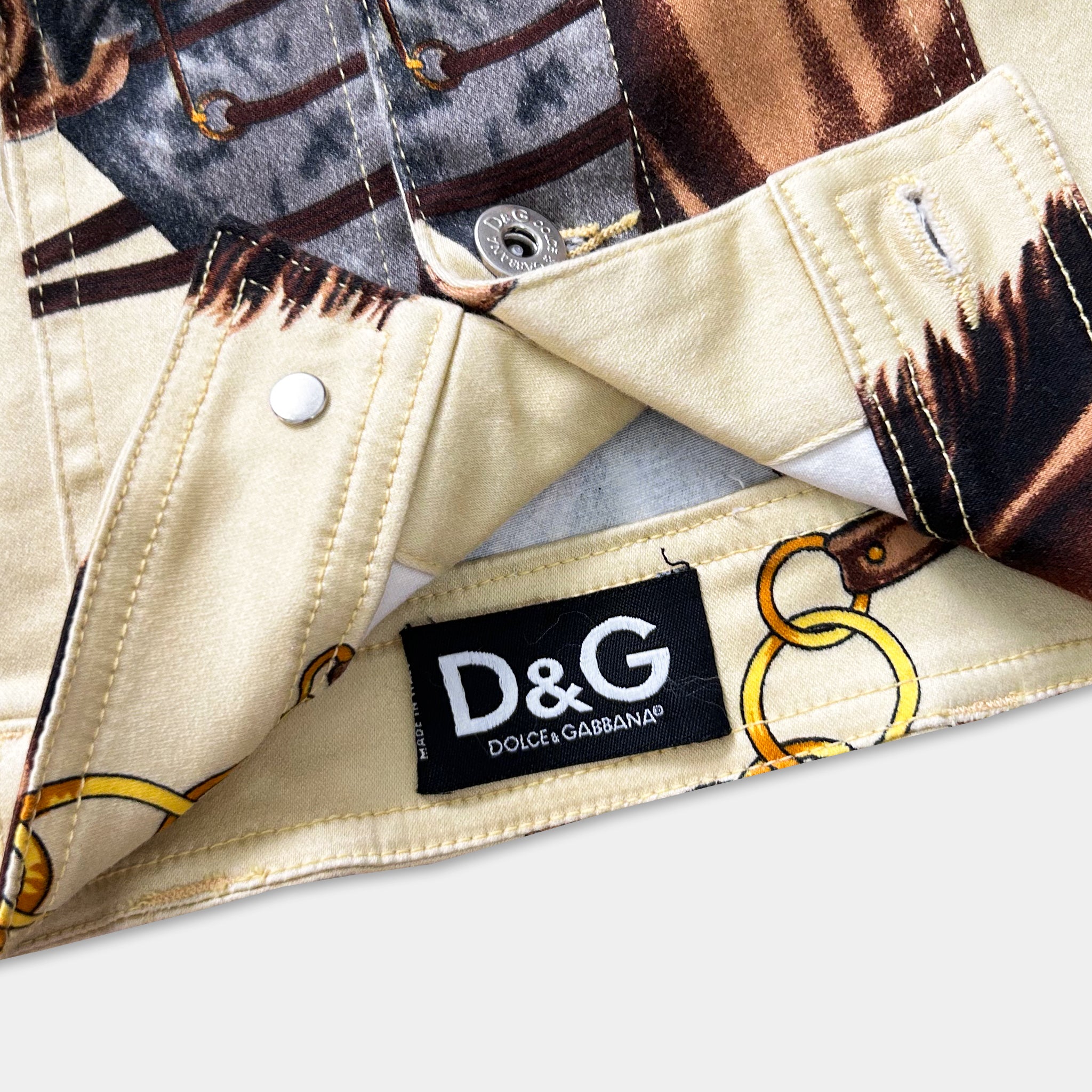 a close-up view of a beige fabric with a pattern of gold rings and a black label with white text that reads "D&G Dolce & Gabbana".