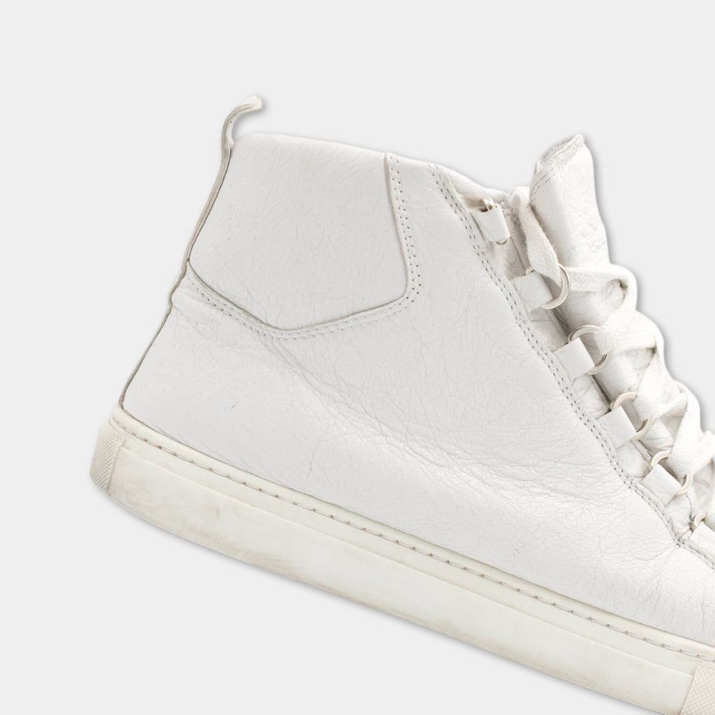 A close-up view of a white high-top sneaker with a lace-up design.