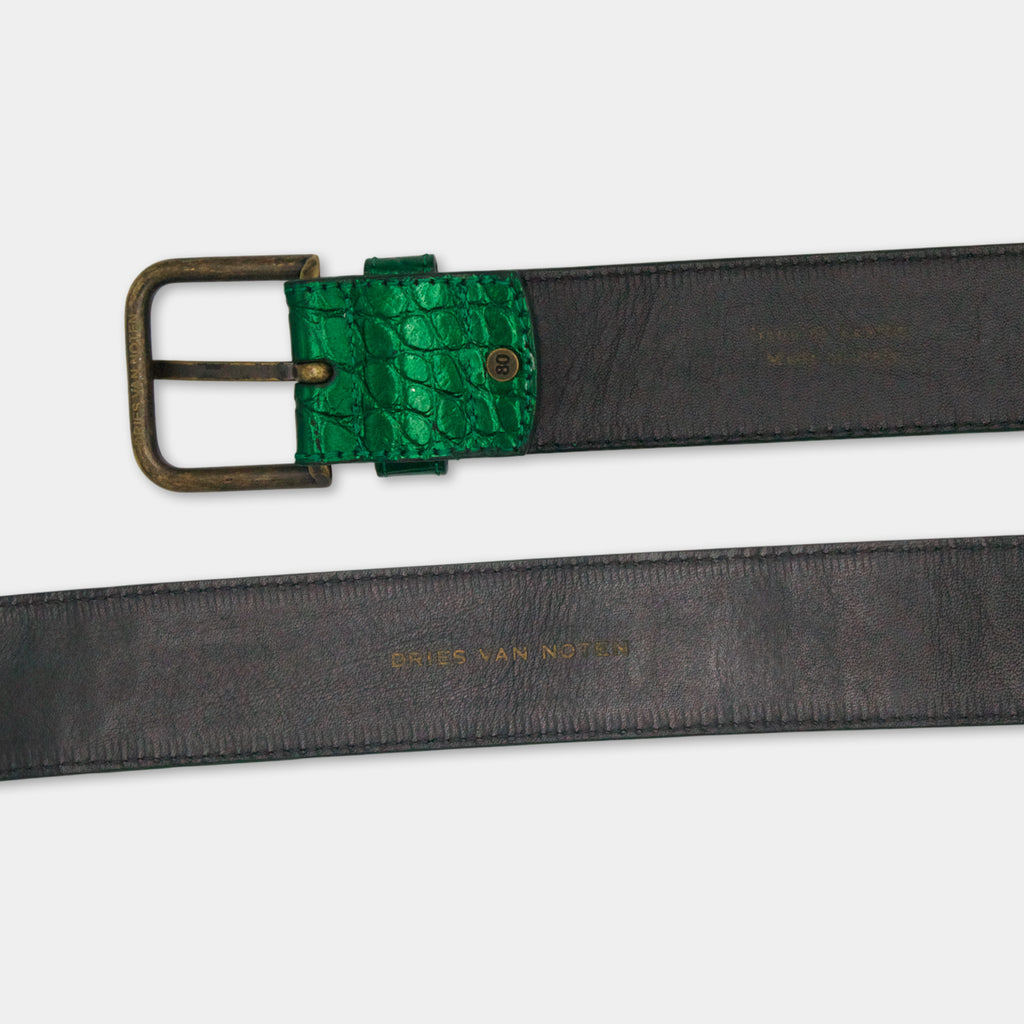 A black leather belt with a green crocodile skin buckle, and the text "DRIES VAN NORTEN" printed on it.
