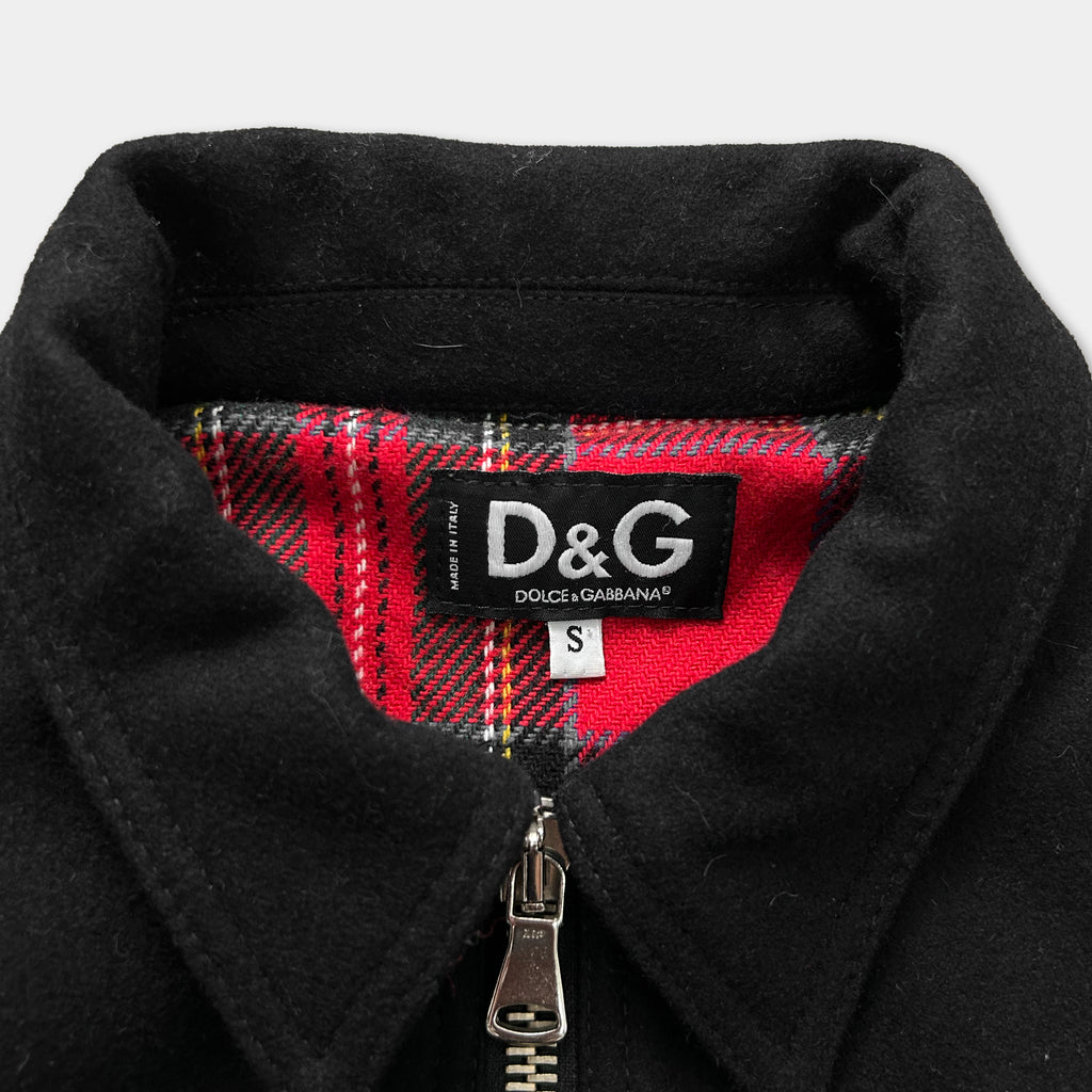 A close-up view of a black jacket with a red and black plaid lining, and a D&G brand label on the collar.