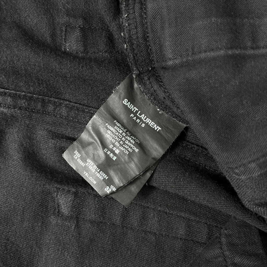 A close-up view of a black fabric, possibly a piece of clothing, with a label attached to it. The label appears to be a label from a clothing brand, specifically Saint Laurent.