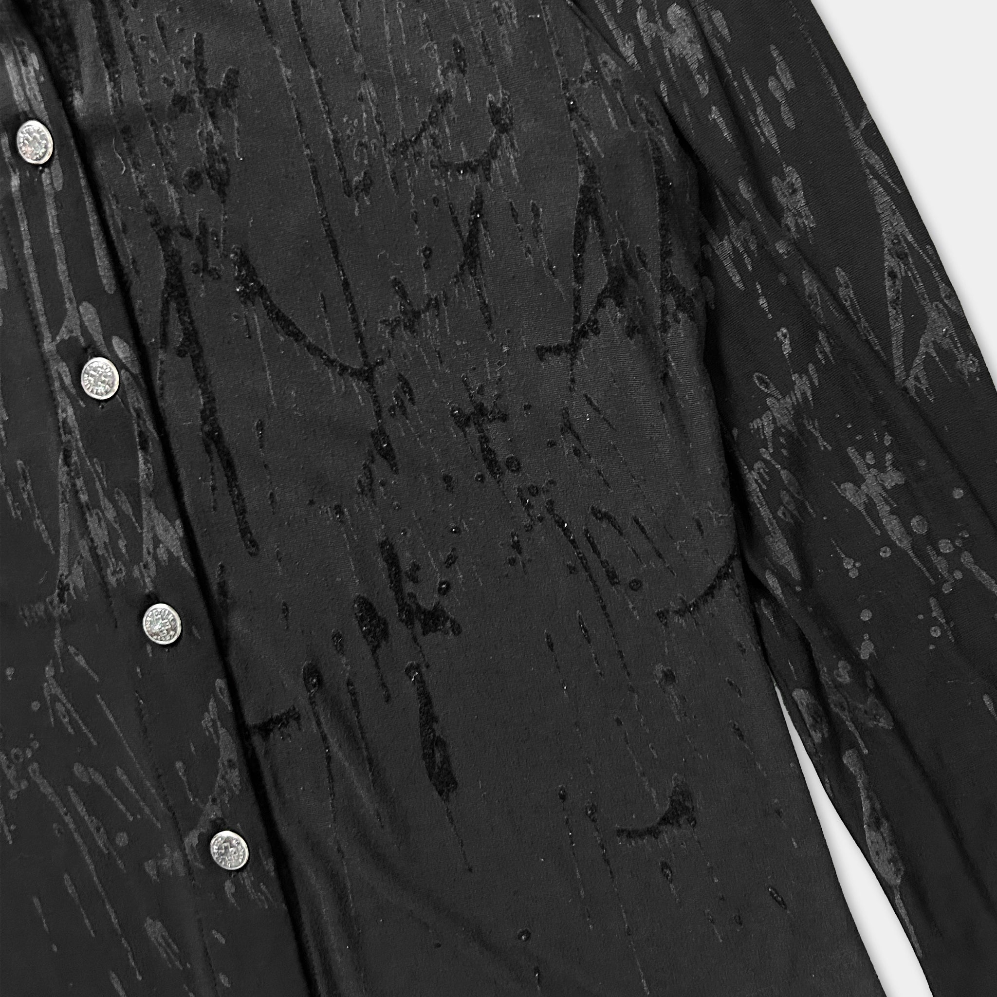 a close-up view of a black fabric with a dark, textured appearance. The fabric appears to be stained or marked, with splotches or drips of liquid or substance visible on the surface.