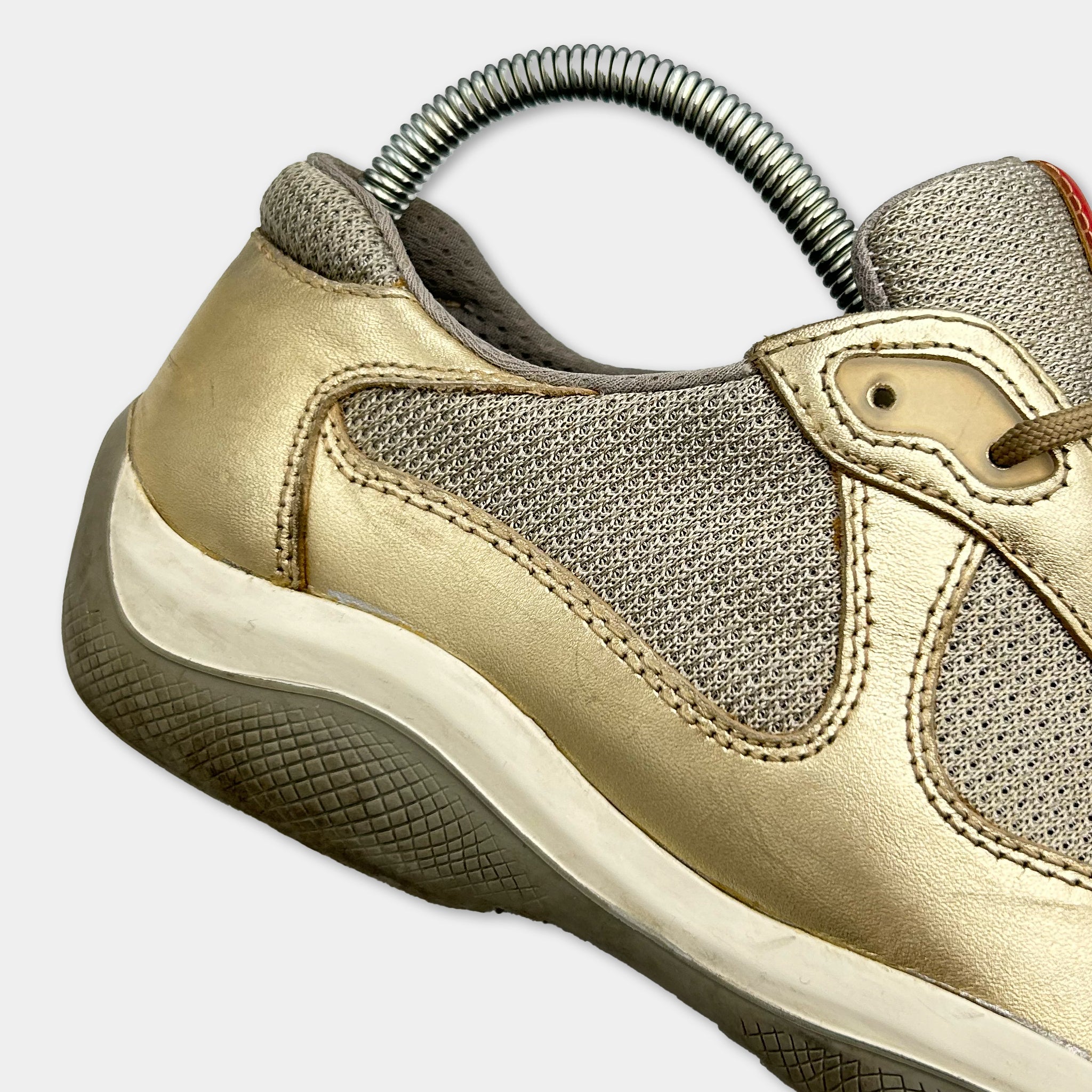 A close-up view of a gold-colored shoe with a metal spring attached to the heel.