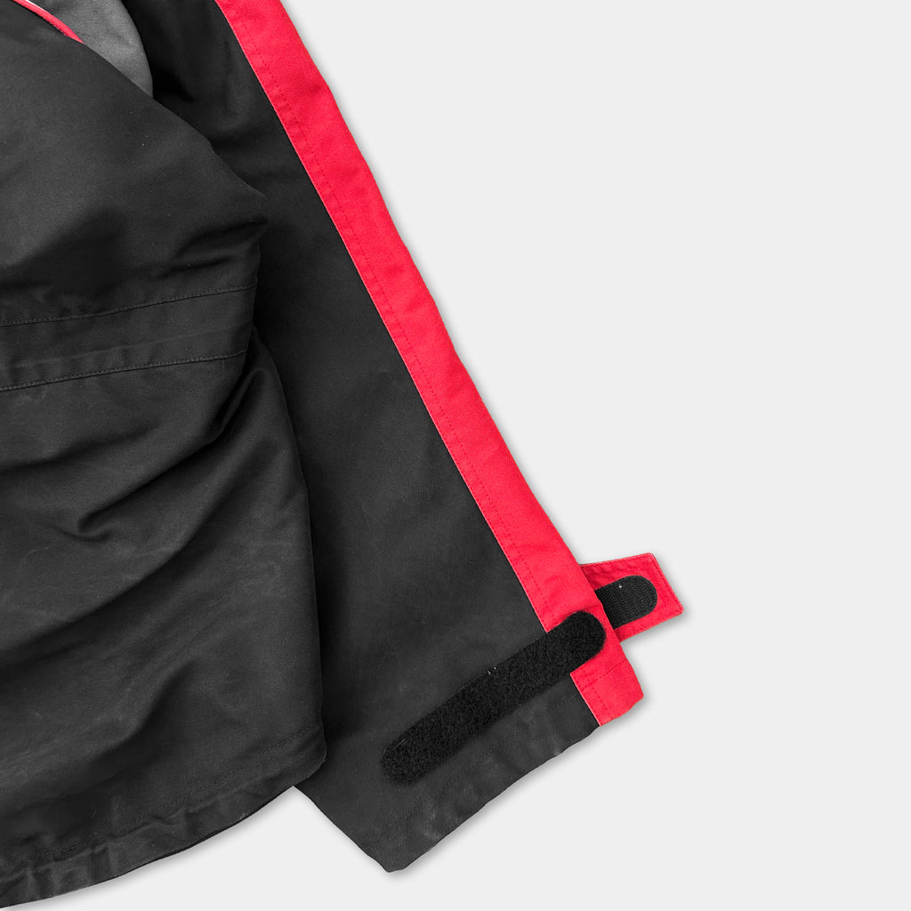 a close-up view of a black and red jacket with a red zipper and a black velcro closure.