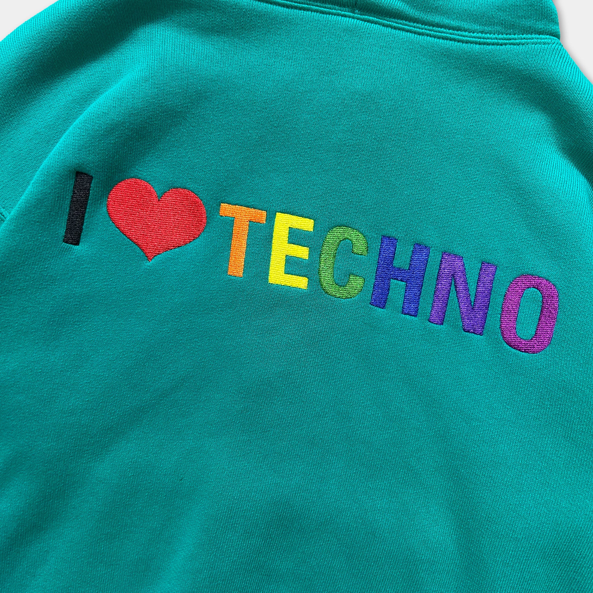 A close-up of a teal-colored hoodie with the text "I ♥ TECHNO" embroidered on it.