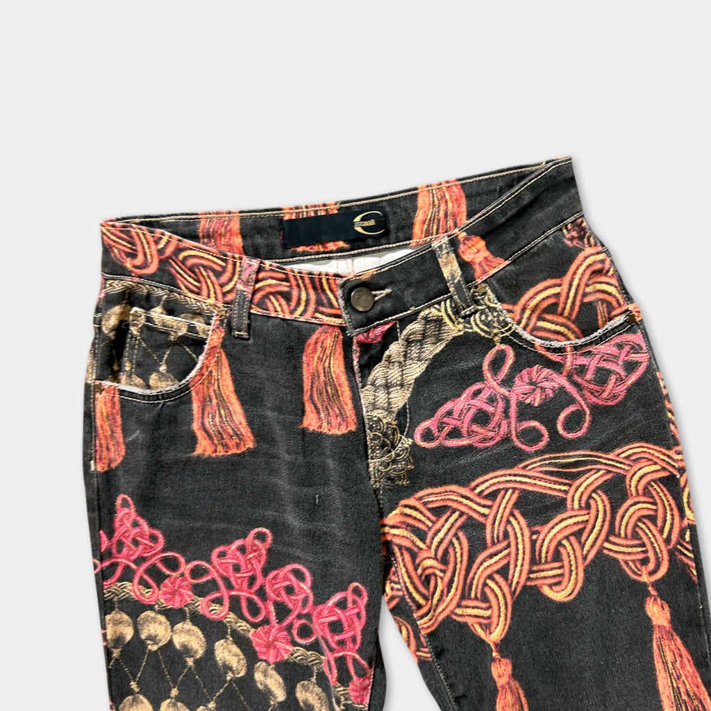 A pair of black jeans with a vibrant, colorful print featuring tassels and floral designs.