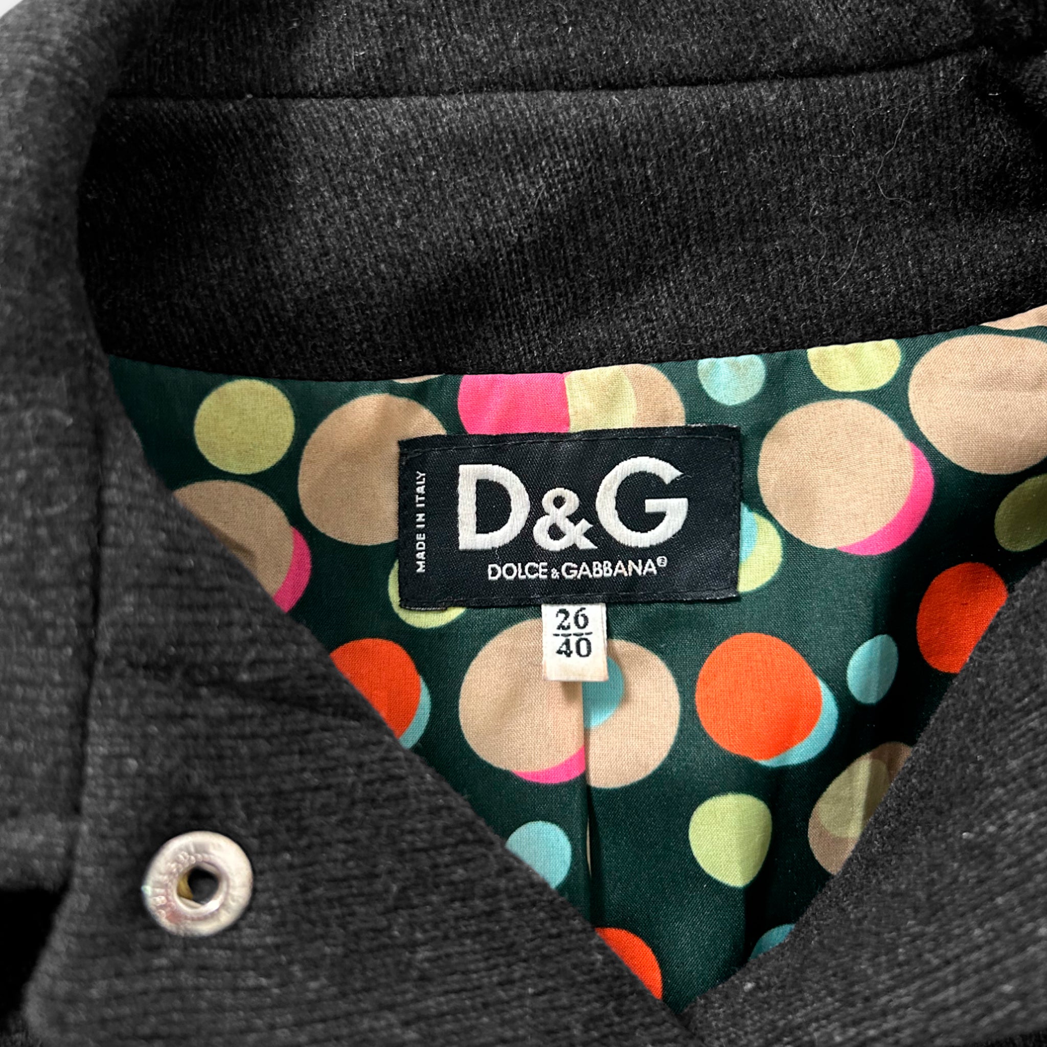 a close-up view of a black jacket with a colorful polka dot pattern inside. The jacket has a label on the inside, indicating it is a D&G product.
