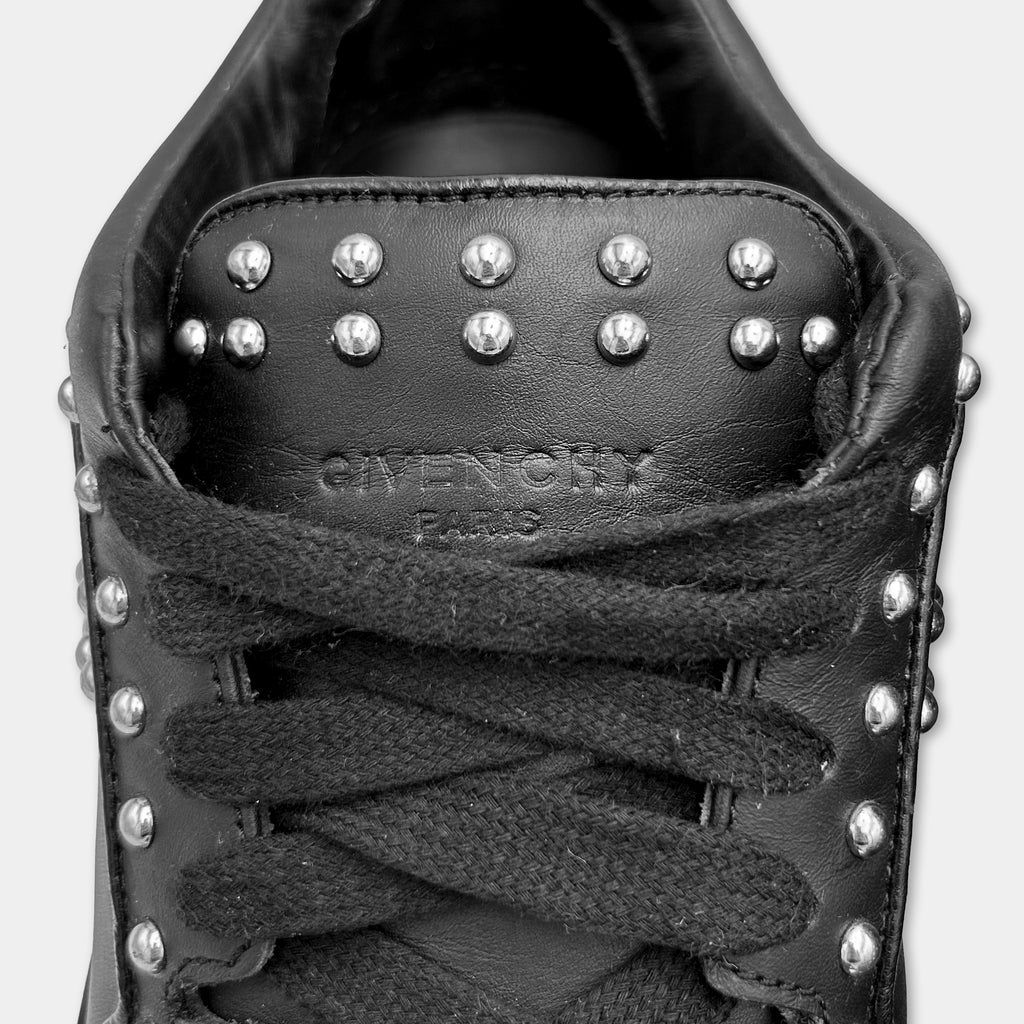 A close-up of a black leather sneaker with silver studs on the top and tongue.