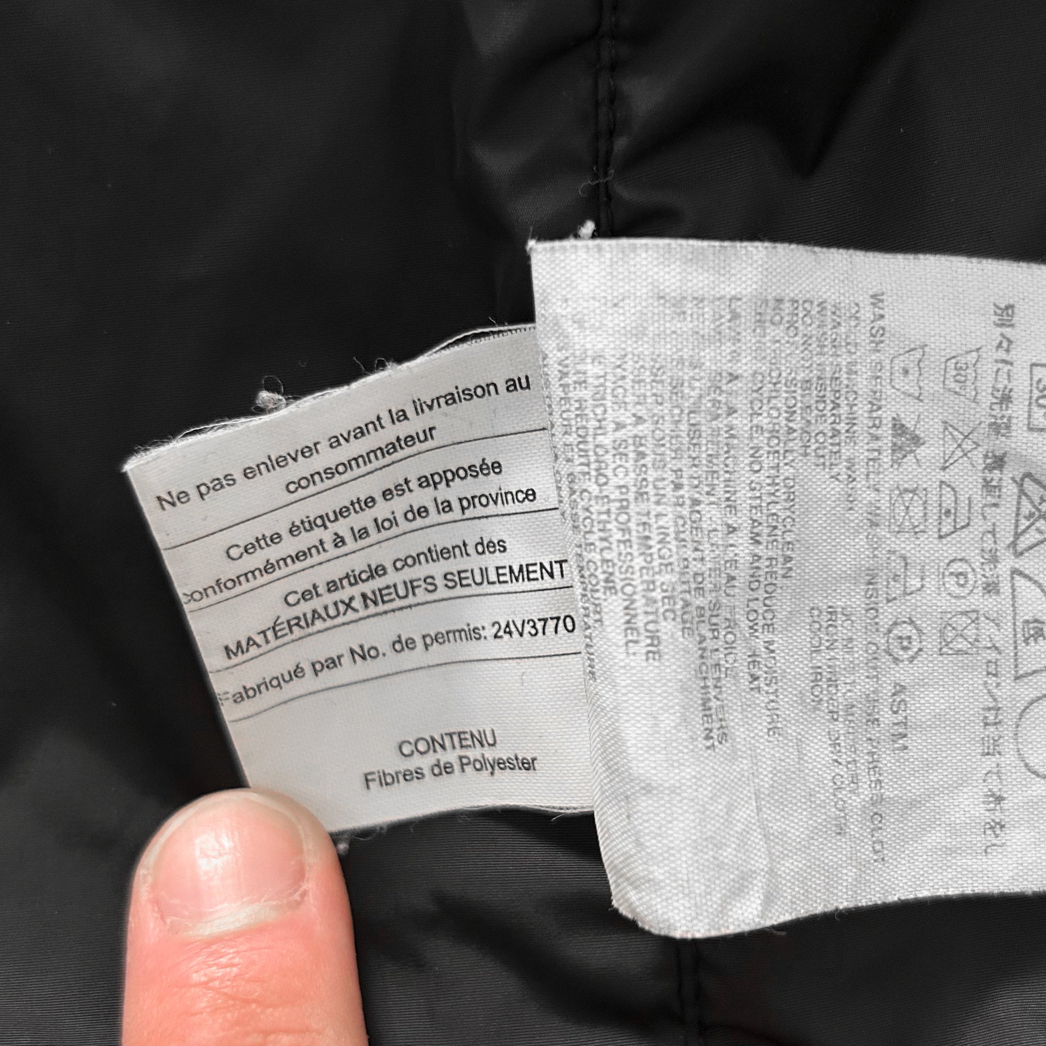 a close-up of a person's finger holding a label with text on it, which appears to be part of a garment or textile product.