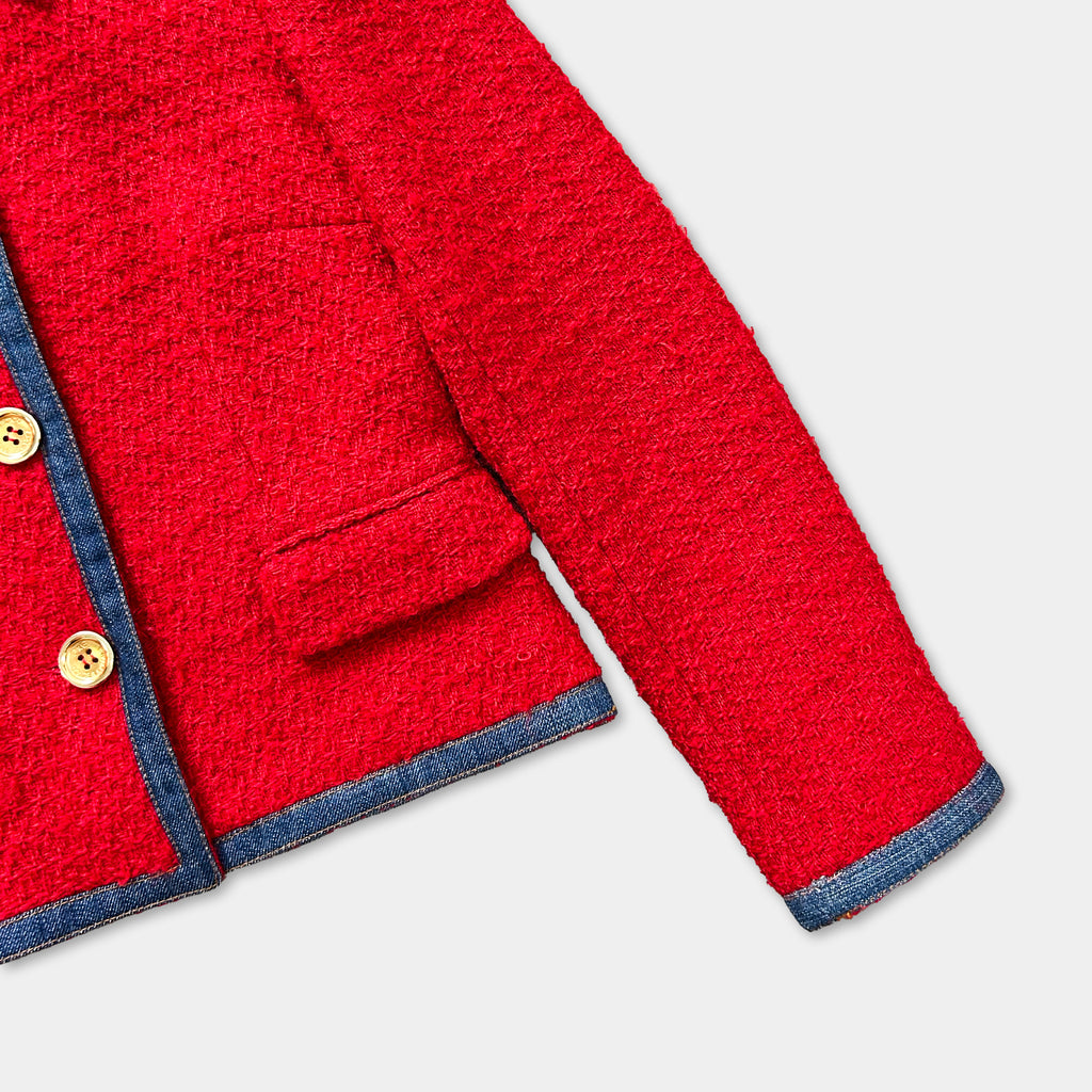 A close-up view of a red tweed jacket with a blue trim, showing the buttons and the fabric texture.