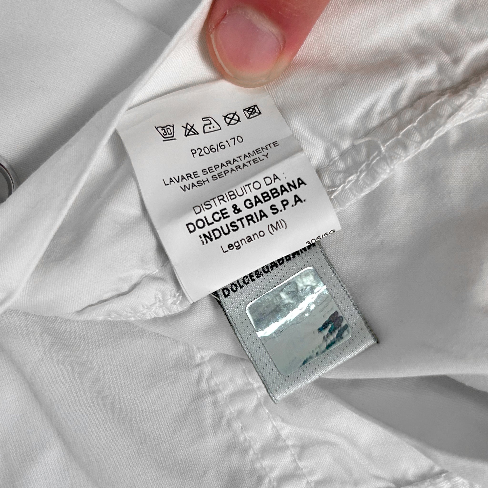 A close-up view of a white garment label with text and symbols, held in someone's hand.