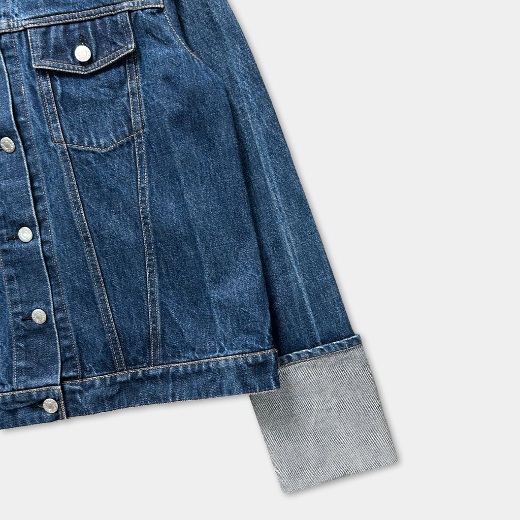 A close-up view of a denim jacket with a button-down front and a gray sleeve.