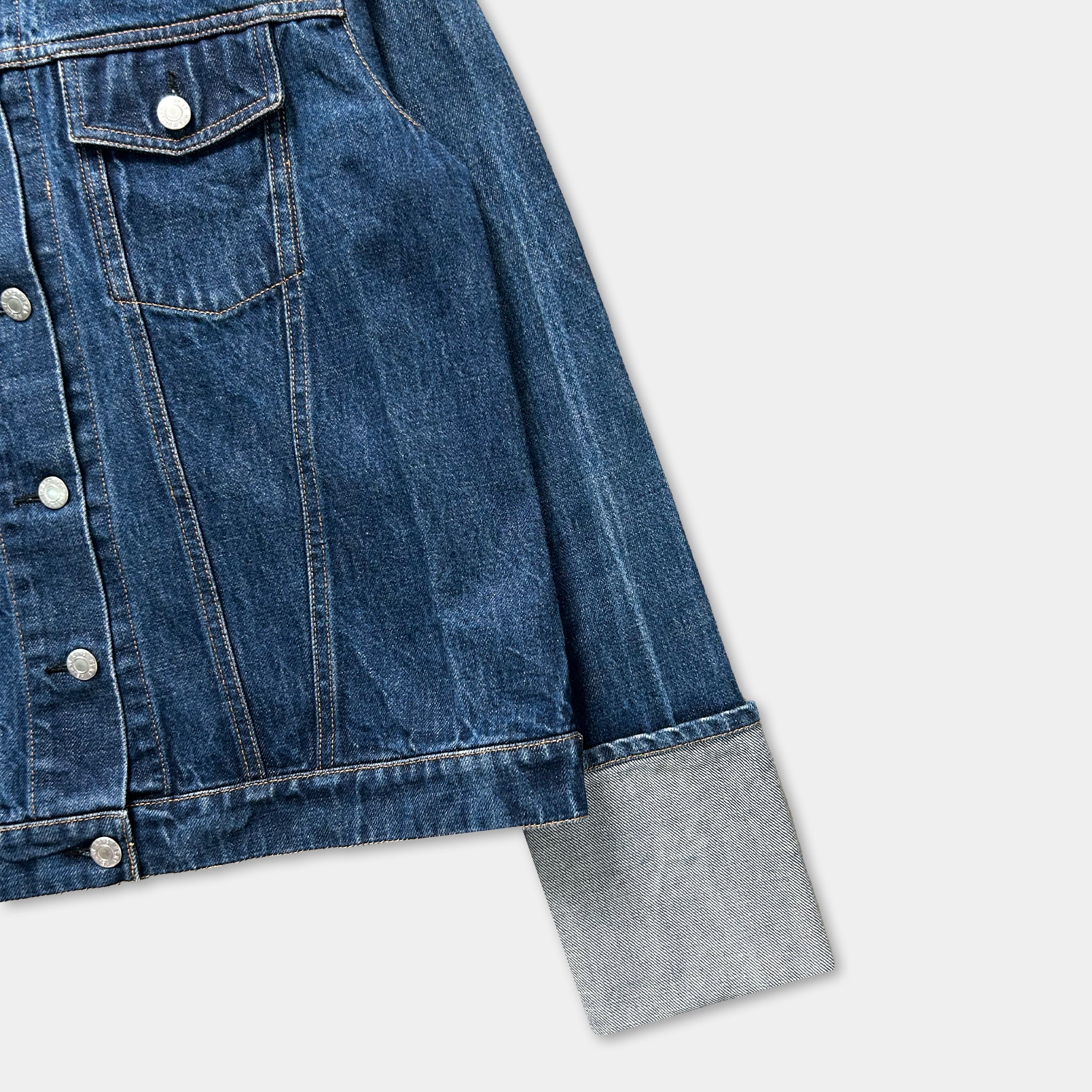 A close-up view of a denim jacket with a button-down front and a gray sleeve.