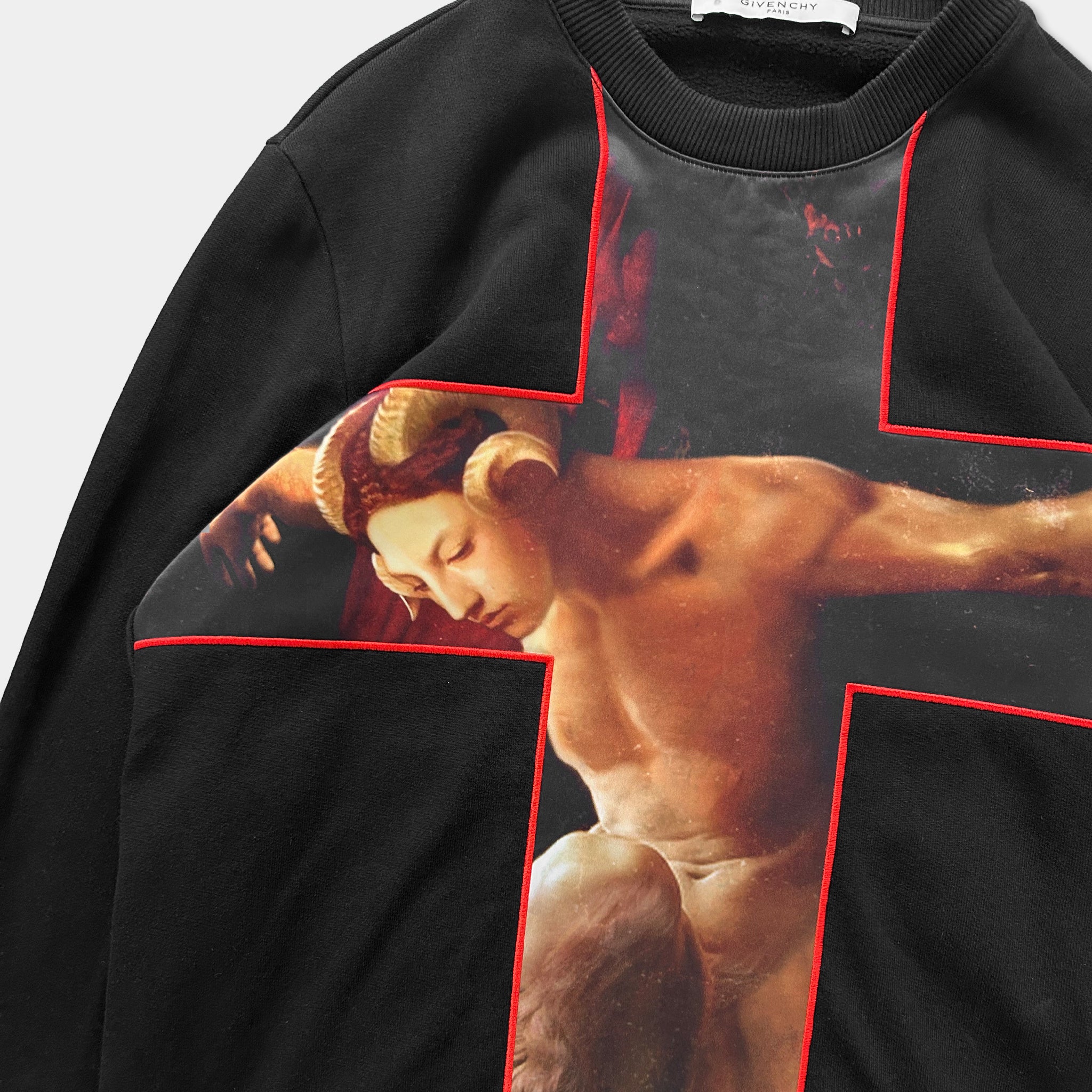 a black sweatshirt with a striking red cross design on the front. The design is a close-up of a nude woman with horns, which is a bold and eye-catching pattern.