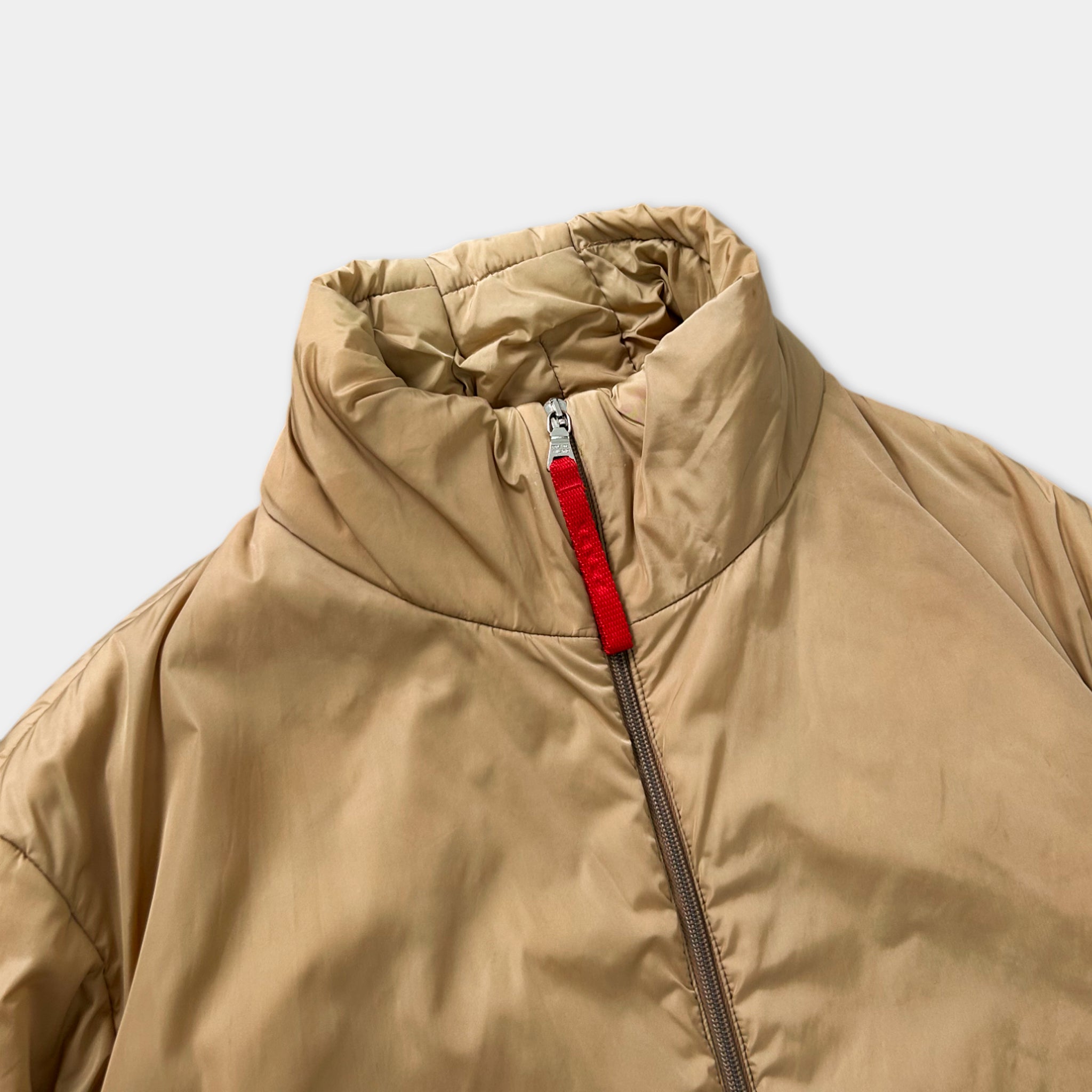 A close-up view of a beige jacket with a red zipper pull.