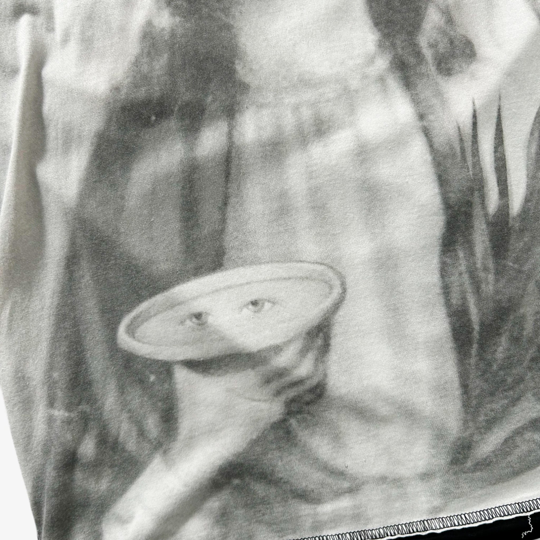 A black and white image showing a person's hand holding a small object, which appears to be a plate or bowl, with a face-like design on the object.