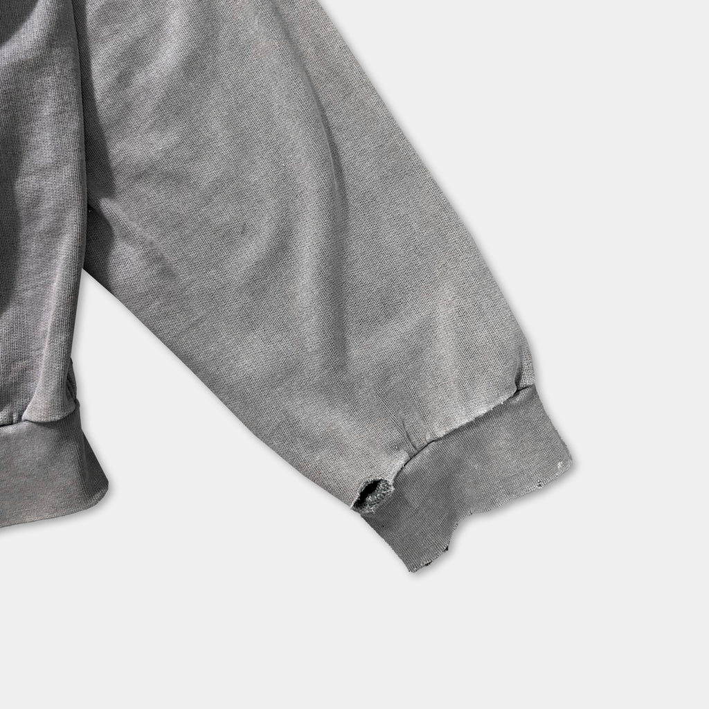 a close-up view of a gray fabric, possibly a sweater or a garment, with a noticeable tear or hole in the sleeve.