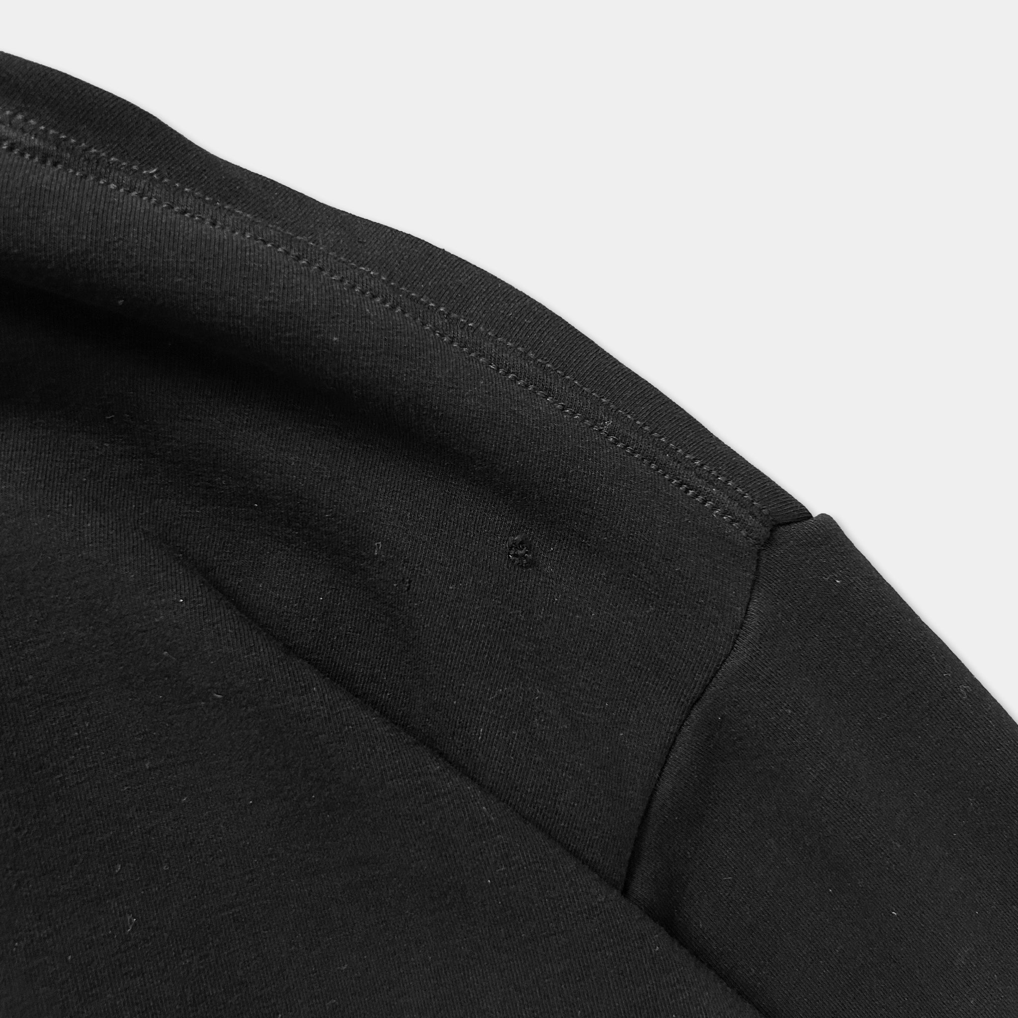 A close-up view of a black fabric, possibly a shirt or sweater, with a small hole or tear visible in the fabric.