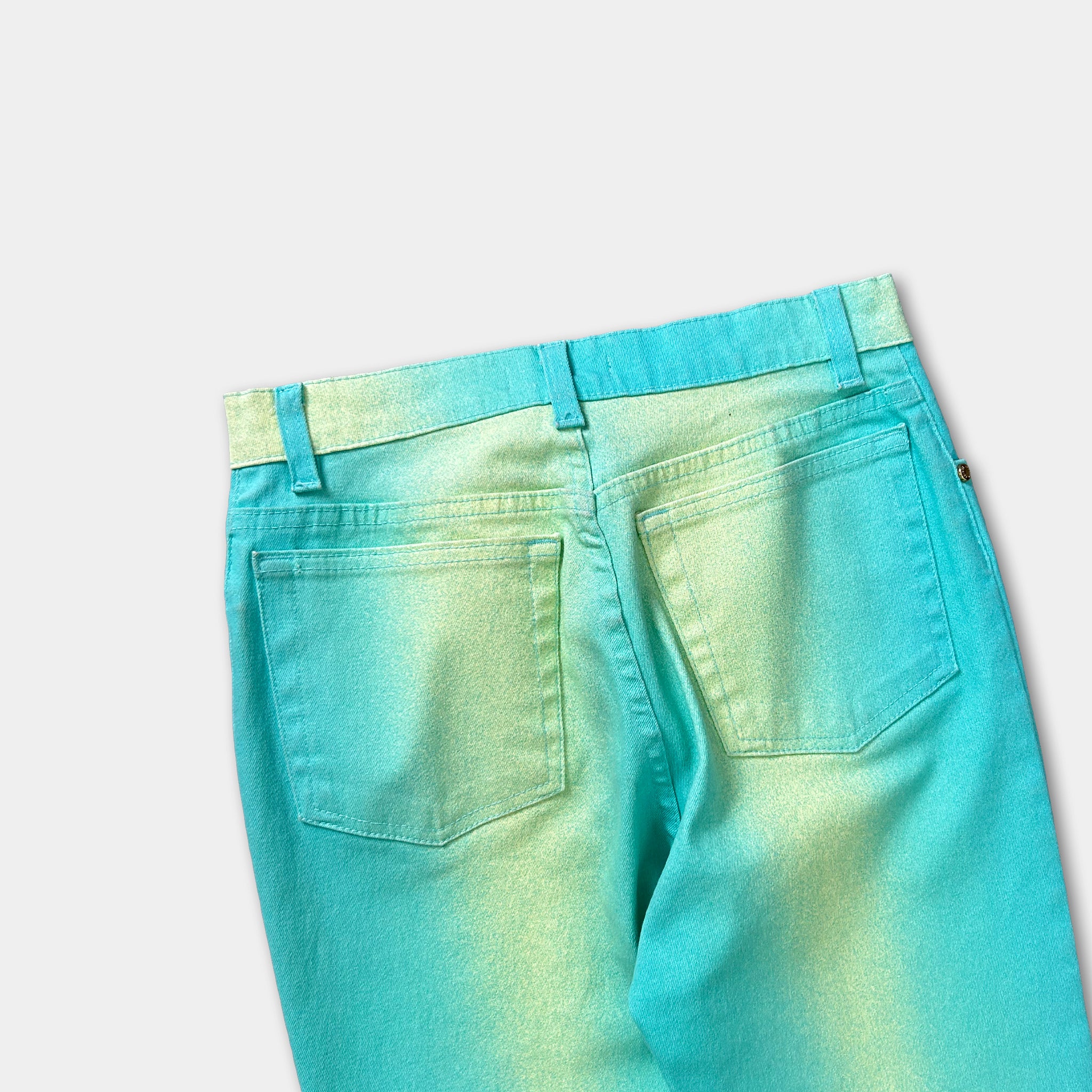 A pair of turquoise-colored jeans with a faded green pattern, displayed against a plain white background.