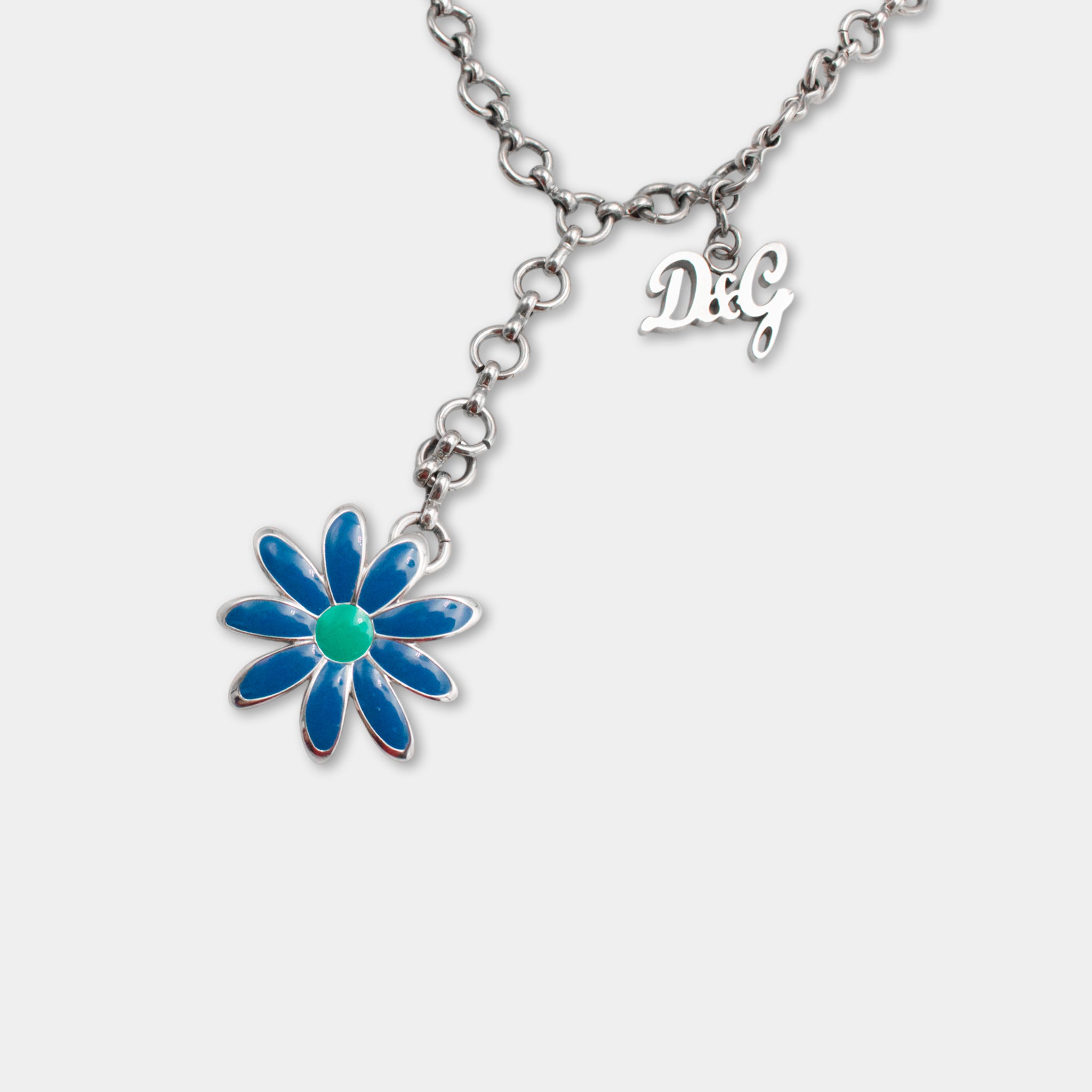 A silver necklace with a blue flower pendant and a small charm with the letters 'D&G' attached to it.