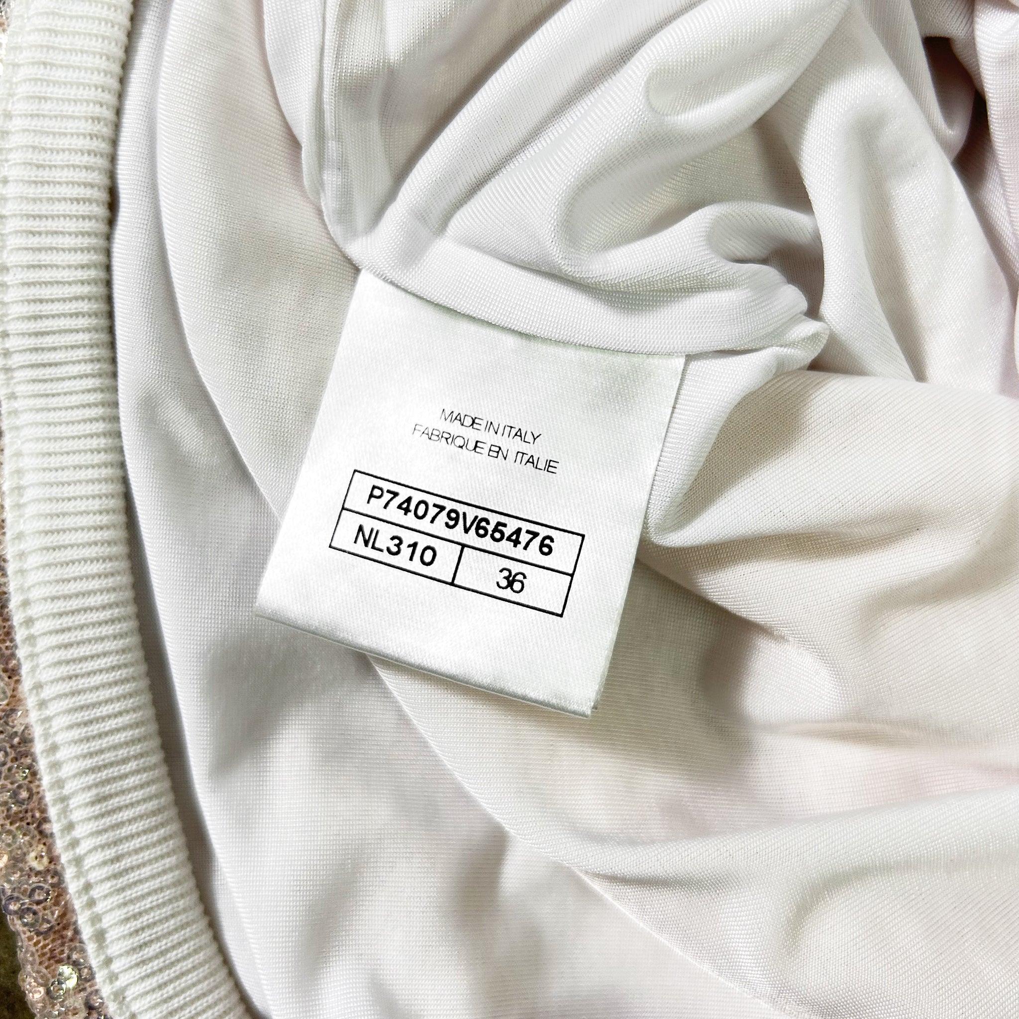 a close-up view of a white fabric, possibly a garment or textile, with a label or tag attached to it. The label appears to contain information about the fabric, such as the brand, material, and size.