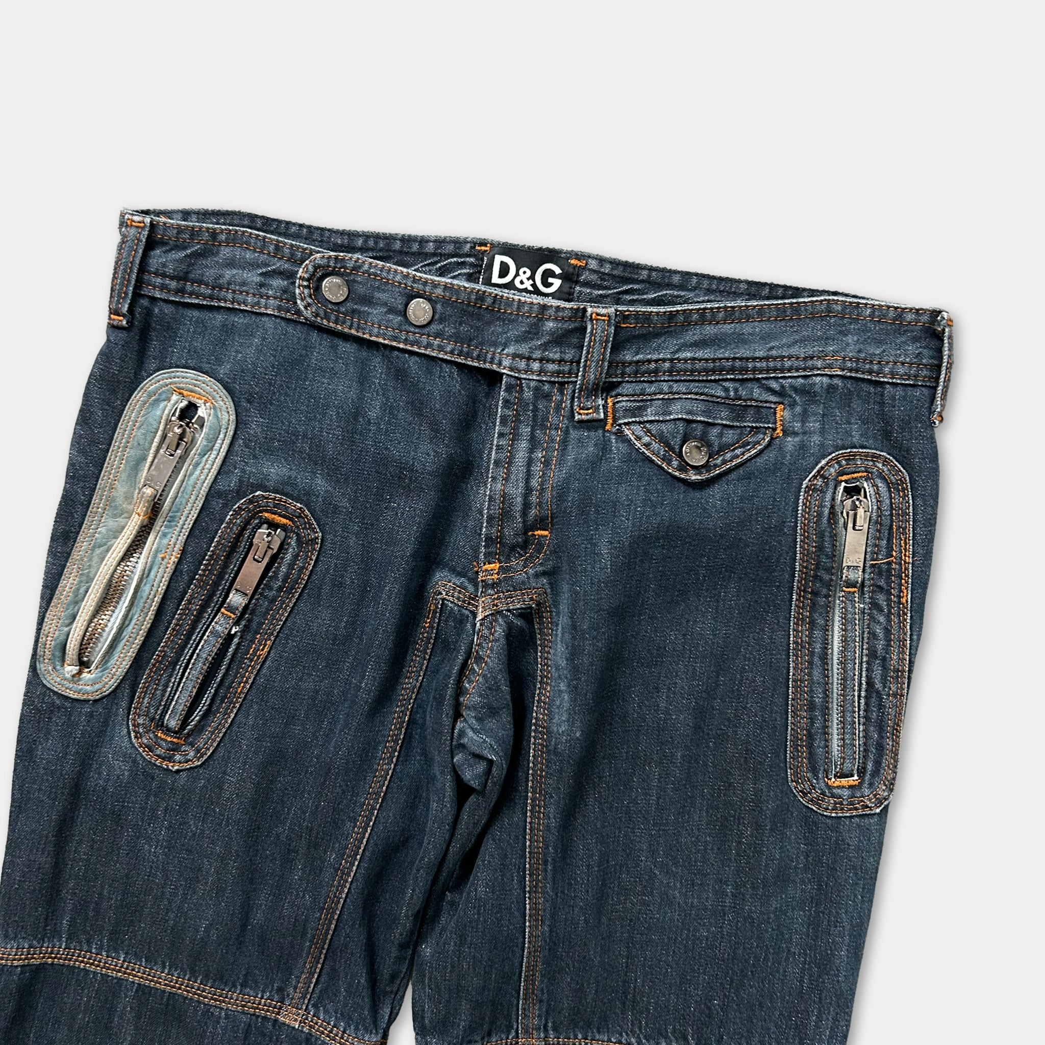 A pair of blue denim jeans with multiple zippers and pockets, including a belt and a pocket on the front.