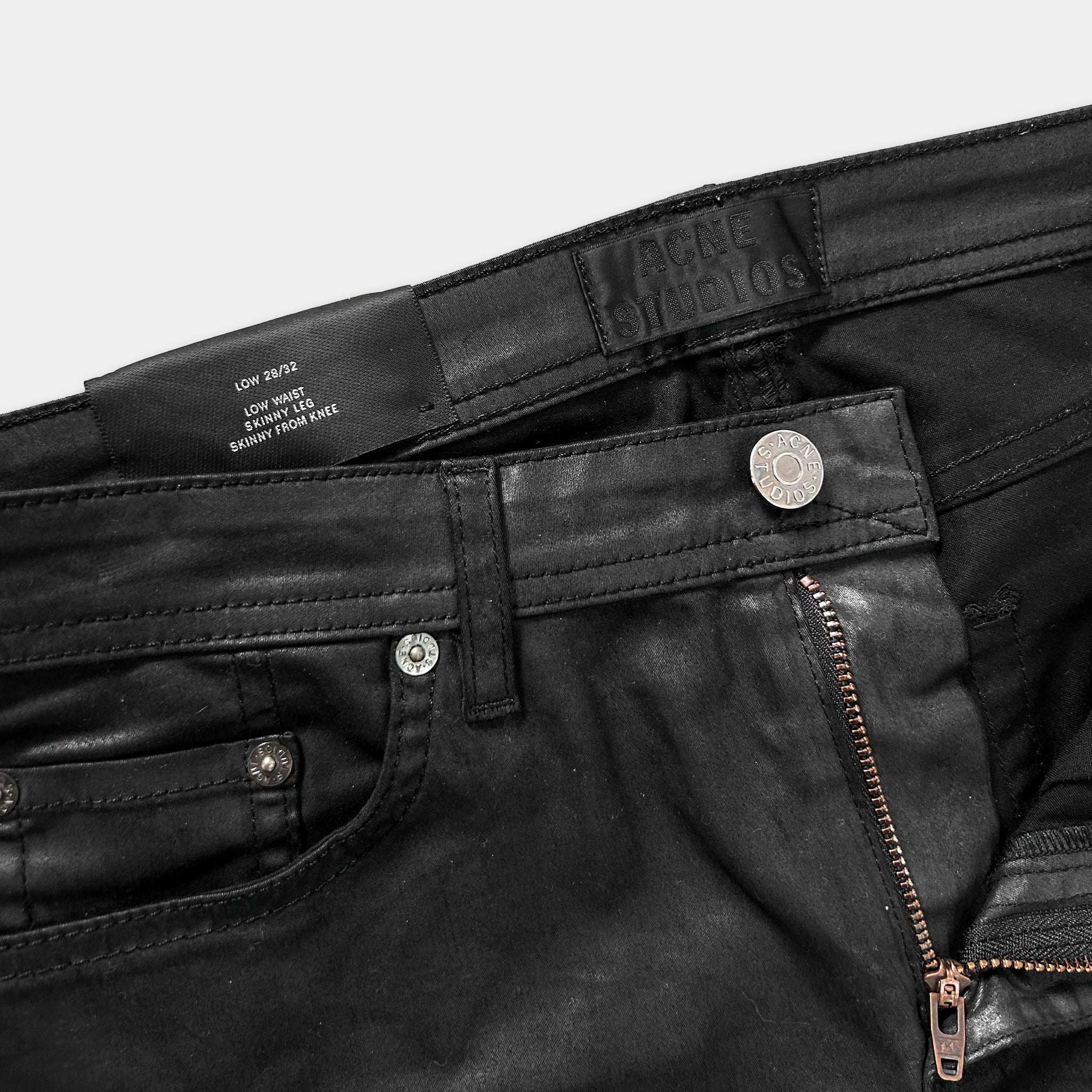 A close-up view of a pair of black skinny jeans, with a label on the waistband and a zipper visible.