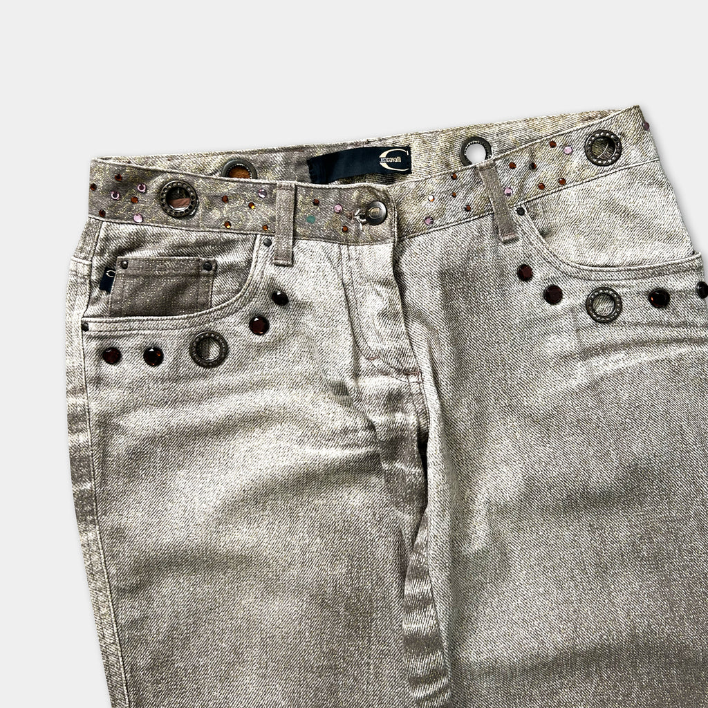 A pair of silver-colored jeans with decorative metal studs on the waistband and pockets.