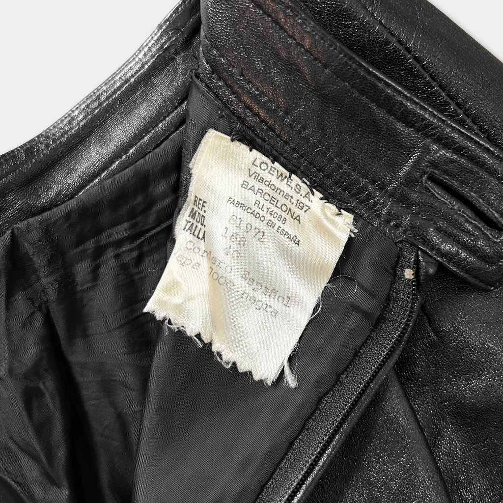 A close-up view of a black leather jacket, showing a label with text and a tear in the fabric.