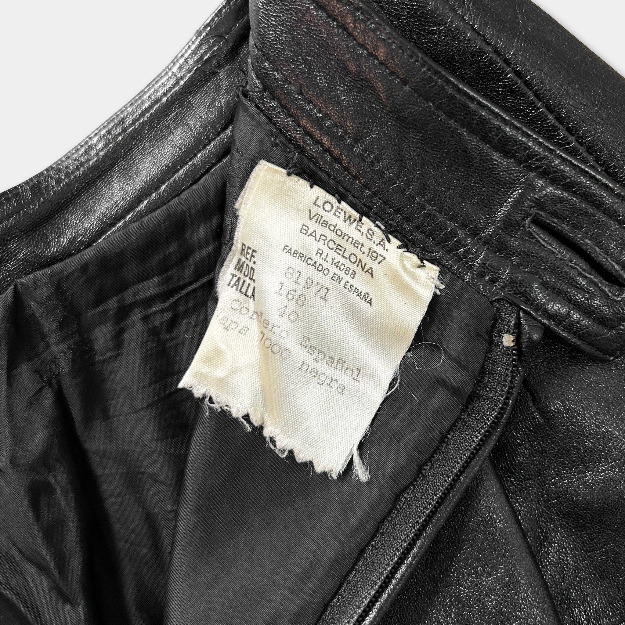 A close-up view of a black leather jacket, showing a label with text and a tear in the fabric.