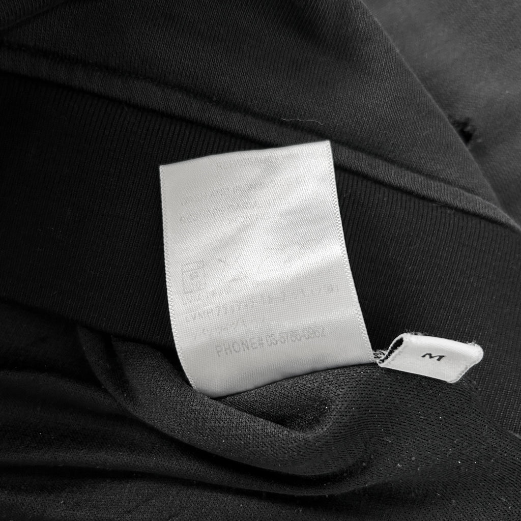 A close-up view of a white label attached to a black fabric, with some text visible on the label.