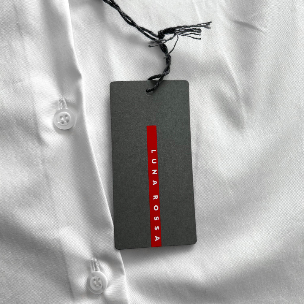 A gray tag with red text is attached to a white shirt, which appears to be a formal or business attire.