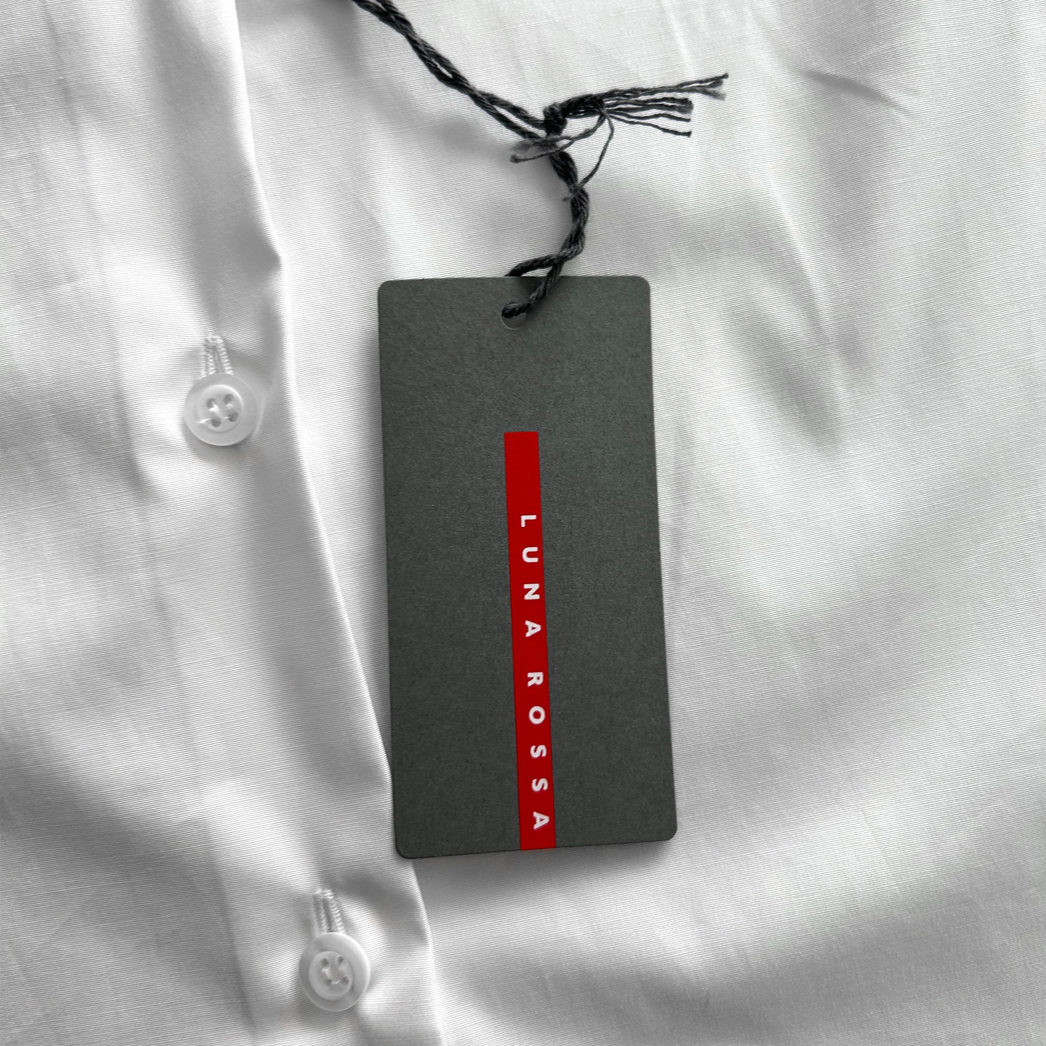 A gray tag with red text is attached to a white shirt, which appears to be a formal or business attire.