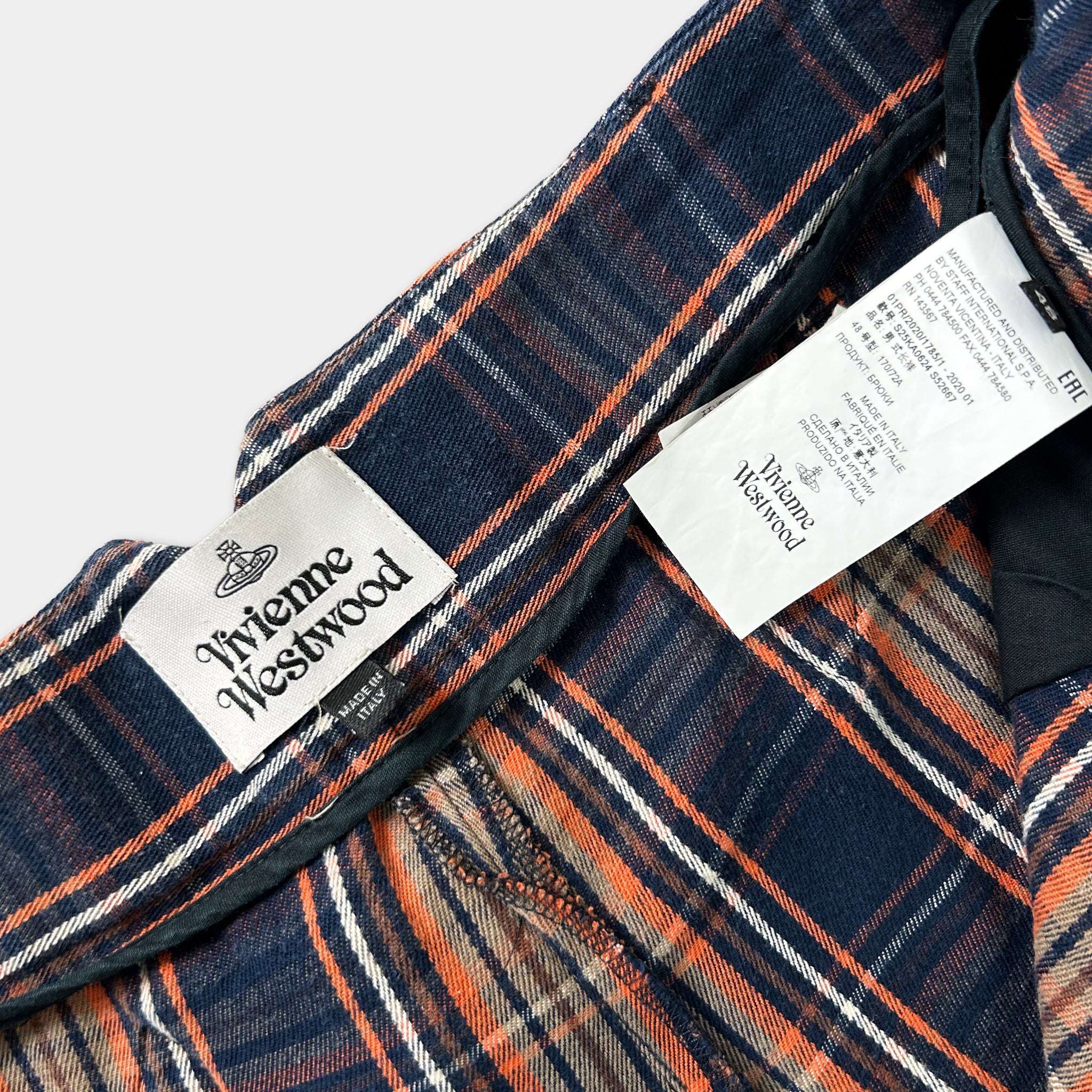 a close-up view of a plaid fabric, possibly a jacket or a shirt, with a label attached to it. The label appears to be from the brand Vivienne Westwood, as indicated by the text on the label.