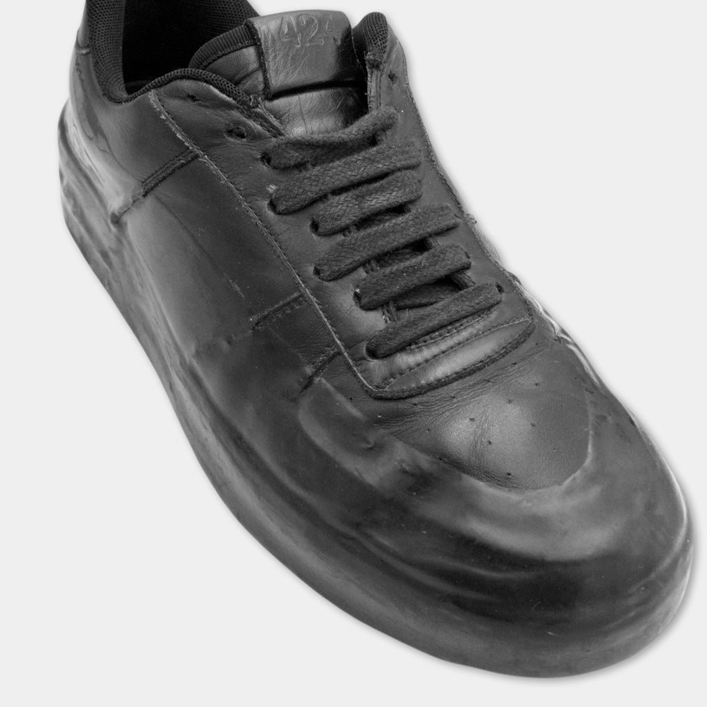 A close-up view of a black, shiny, and glossy shoe with a black sole and laces.