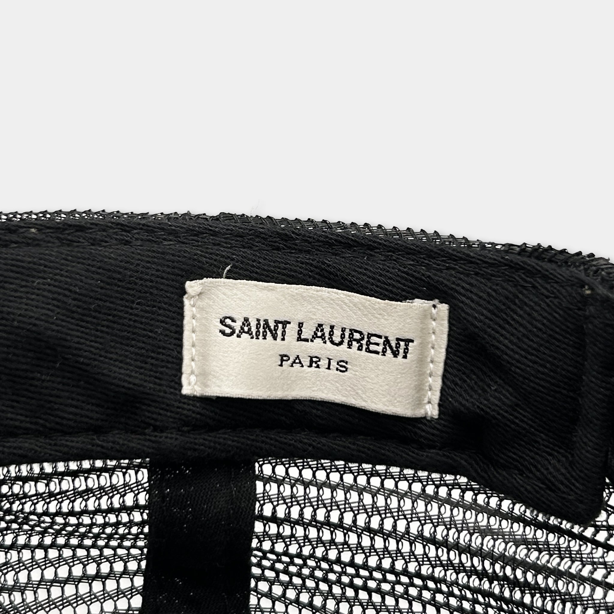 A close-up view of a black mesh fabric with a white label that reads "SAINT LAURENT PARIS" printed on it.