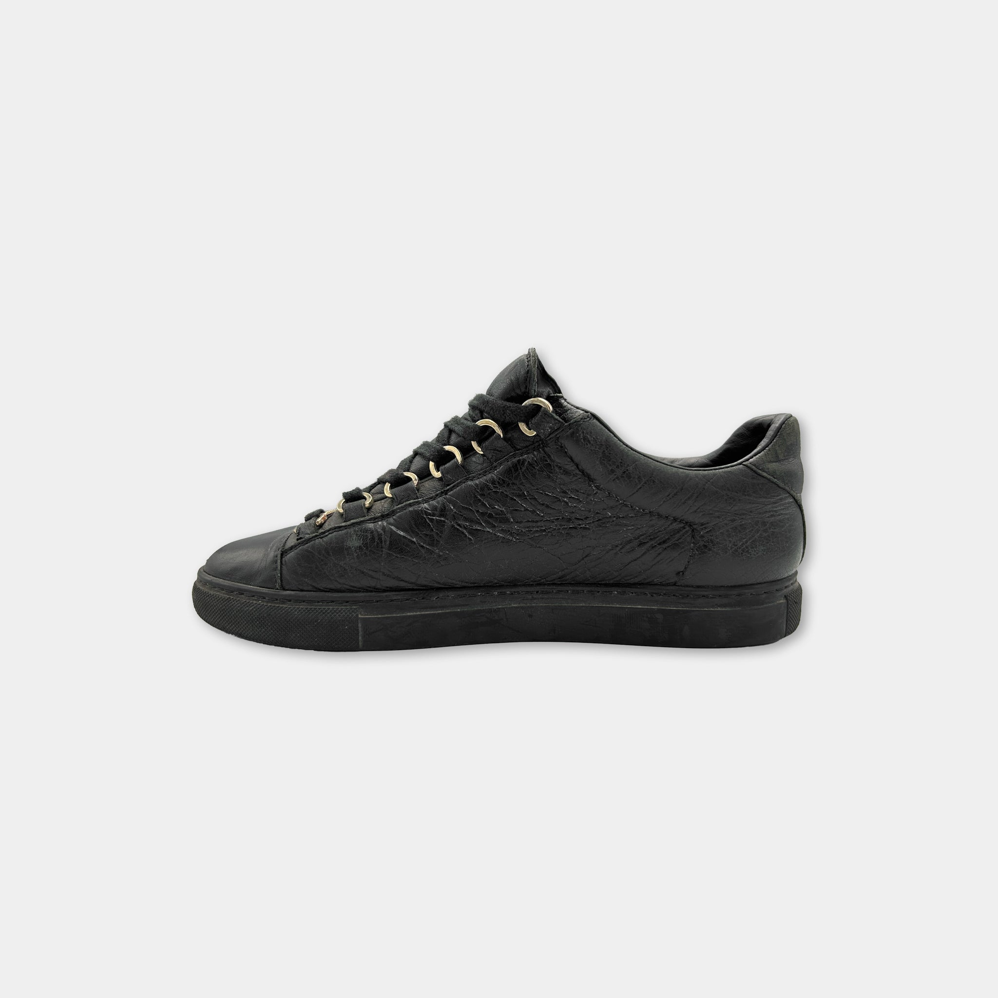 A black leather sneaker with gold-colored laces and soles.