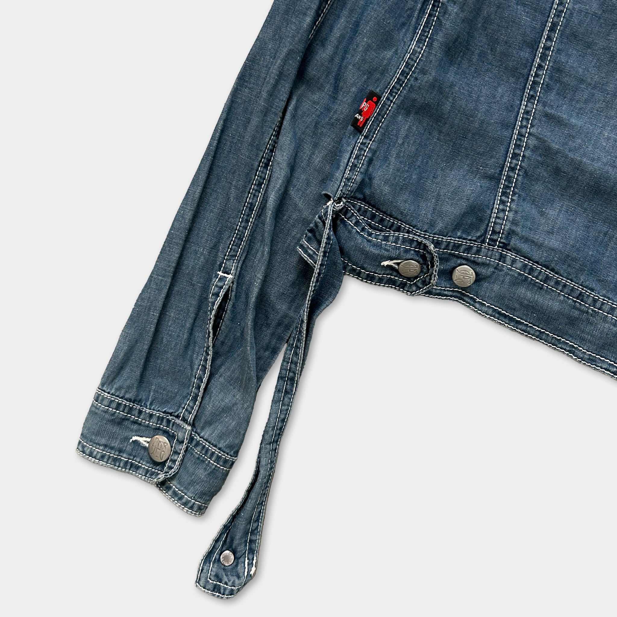 A close-up view of a denim jacket with a red tag visible on the back pocket.