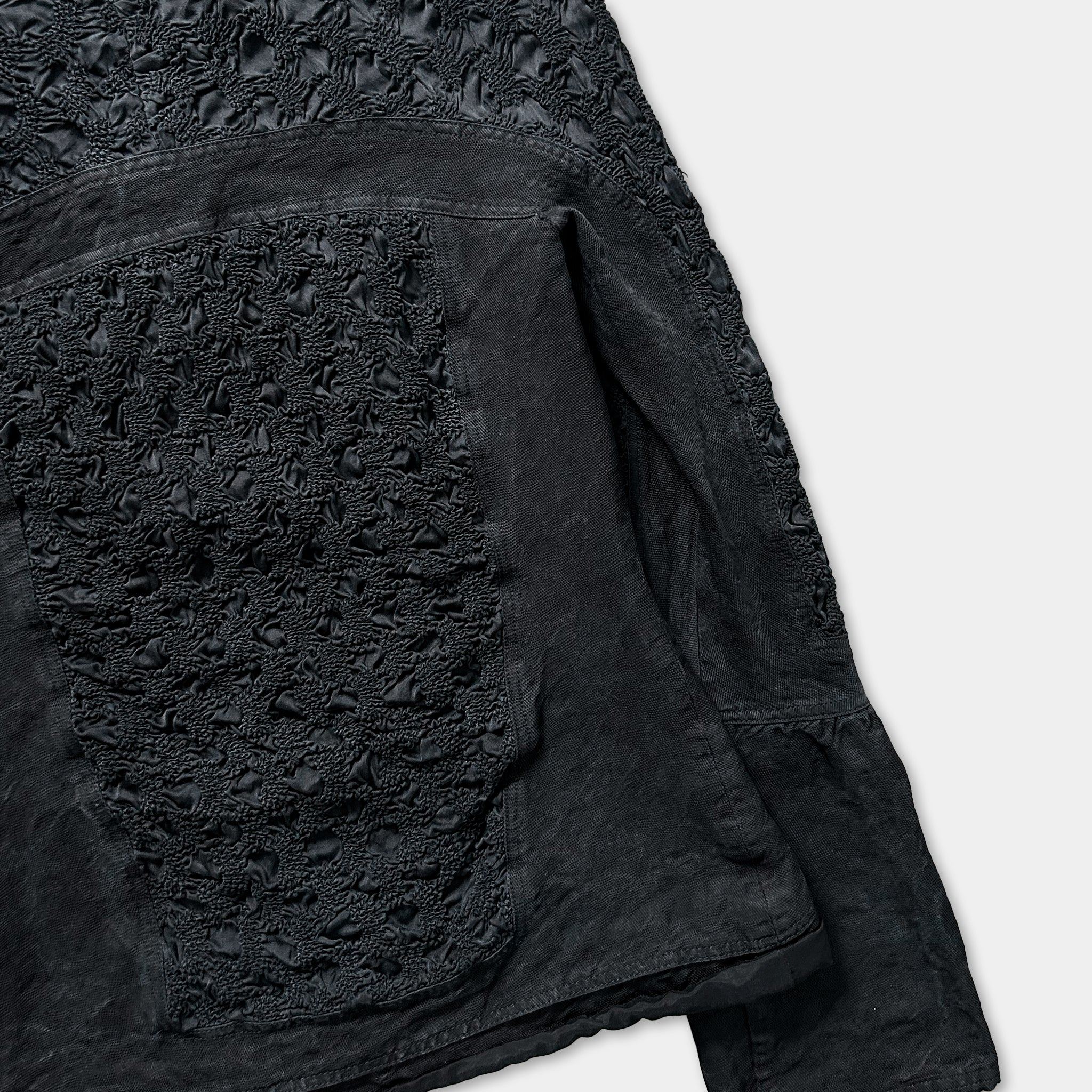 a close-up view of a black fabric with a lace-like pattern, featuring a pocket-like design.