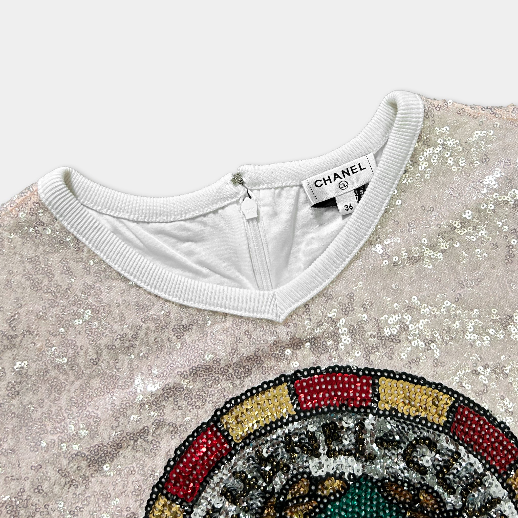 a close-up view of a white collar with a zipper, and a colorful, sequined design on the front of the shirt.